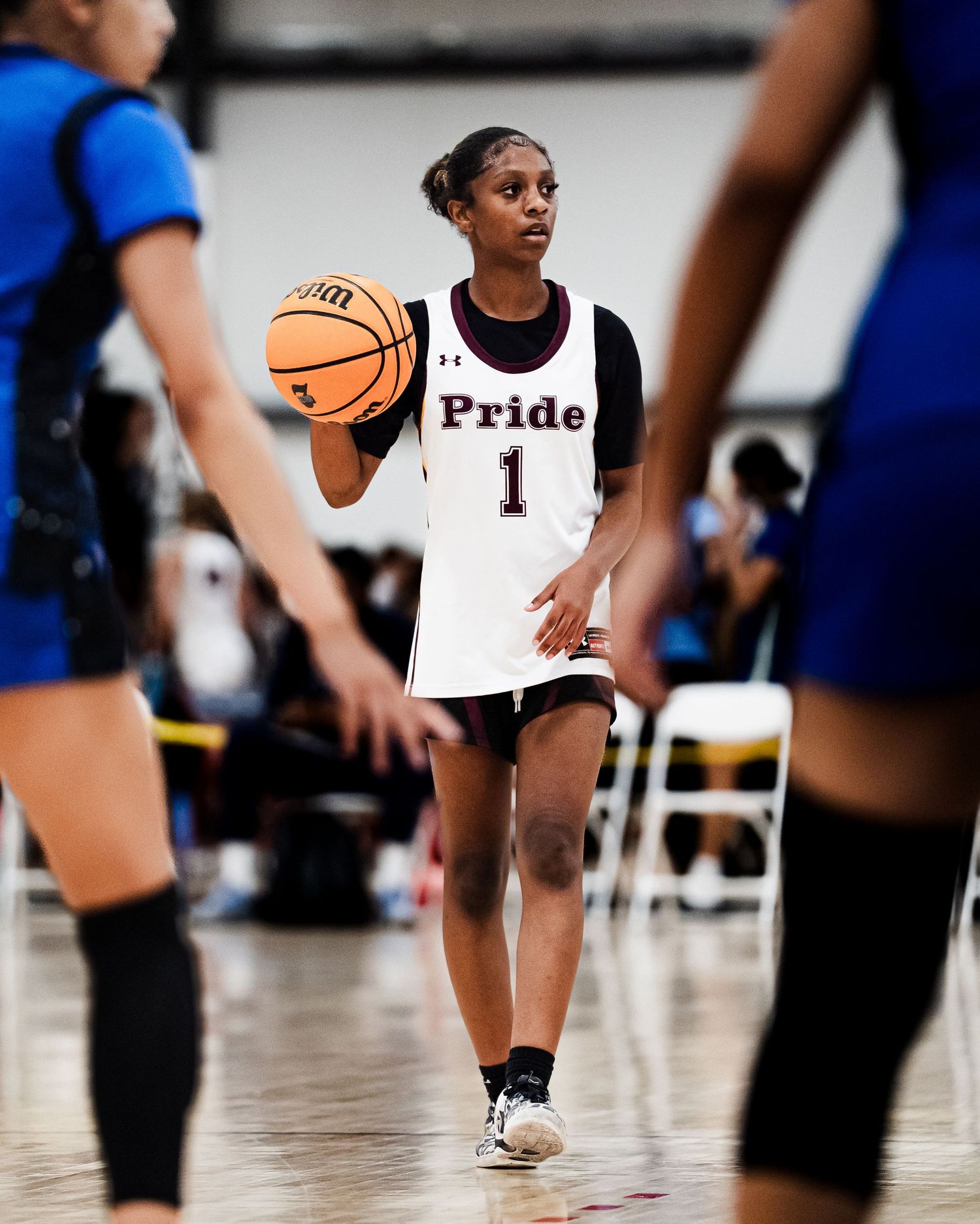 Female basketball player wearing Pride number 1 jersey dribbles the ball during an indoor basketball game.