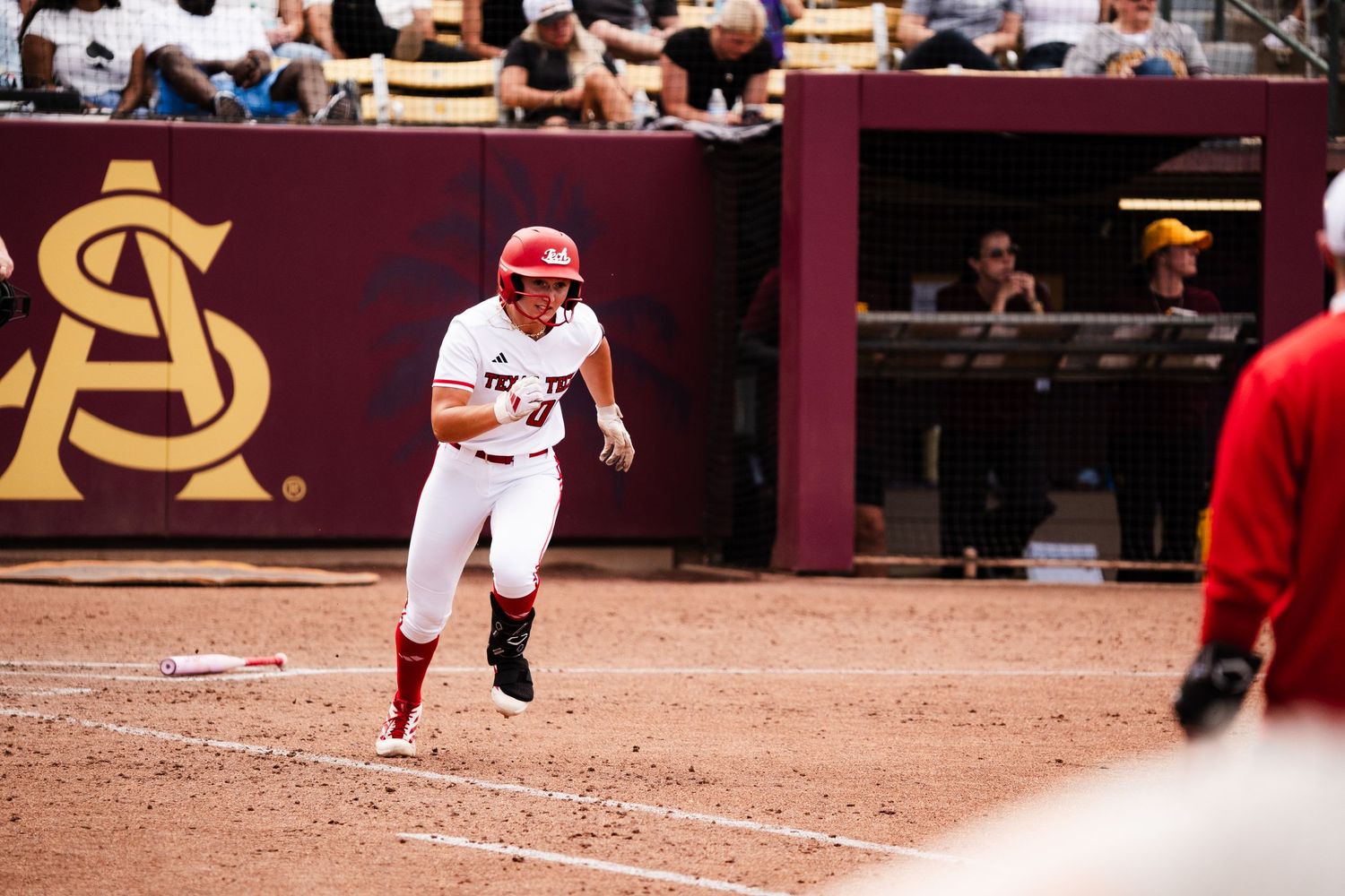 A softball player in red uniform rounds the bases at an Arizona State University home game.