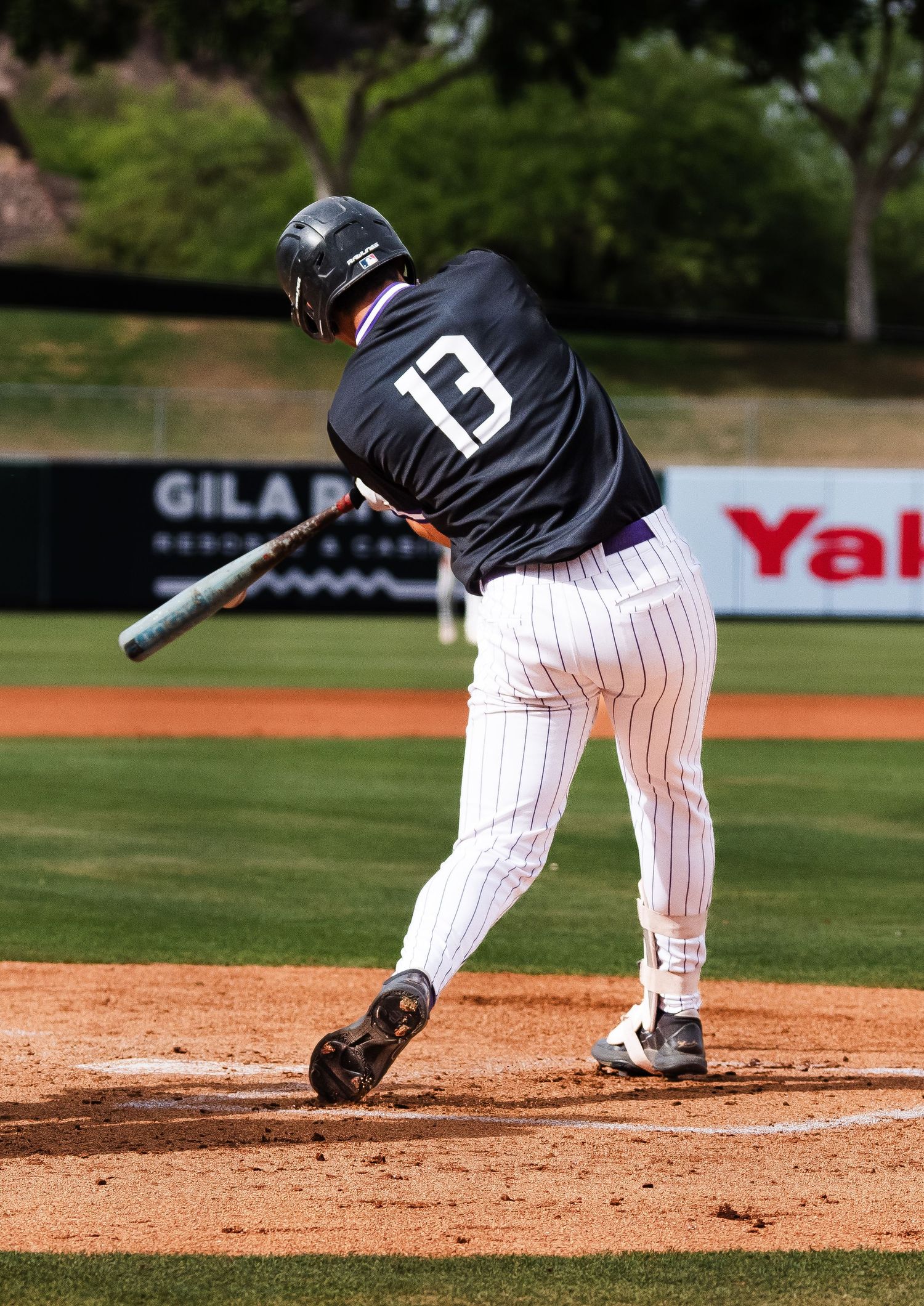 Baseball player #13 in black pinstripe uniform making contact with pitch during college baseball game.
