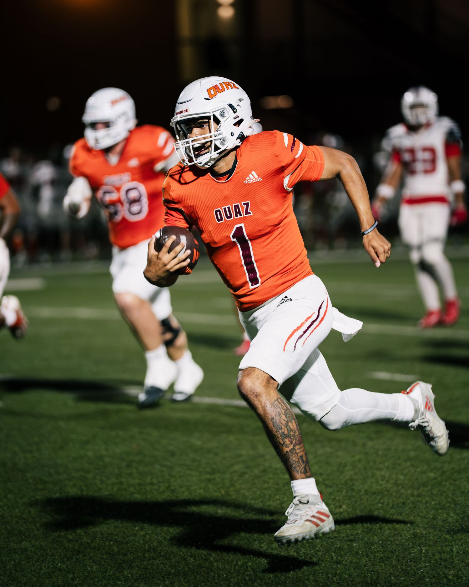 Player #1 in orange Duaz football jersey runs with ball during night game.