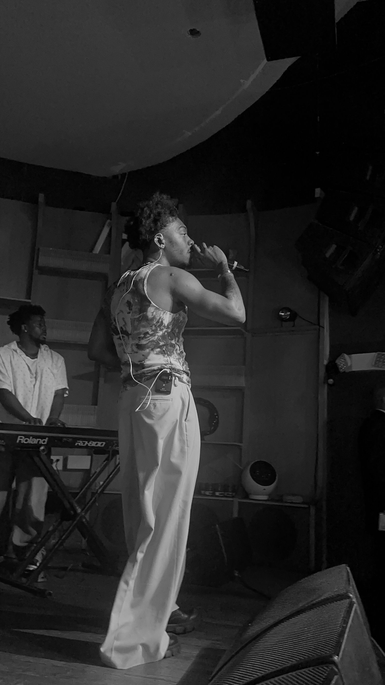 Black and white photo of a female singer performing on stage with a keyboardist playing a Roland keyboard behind her.