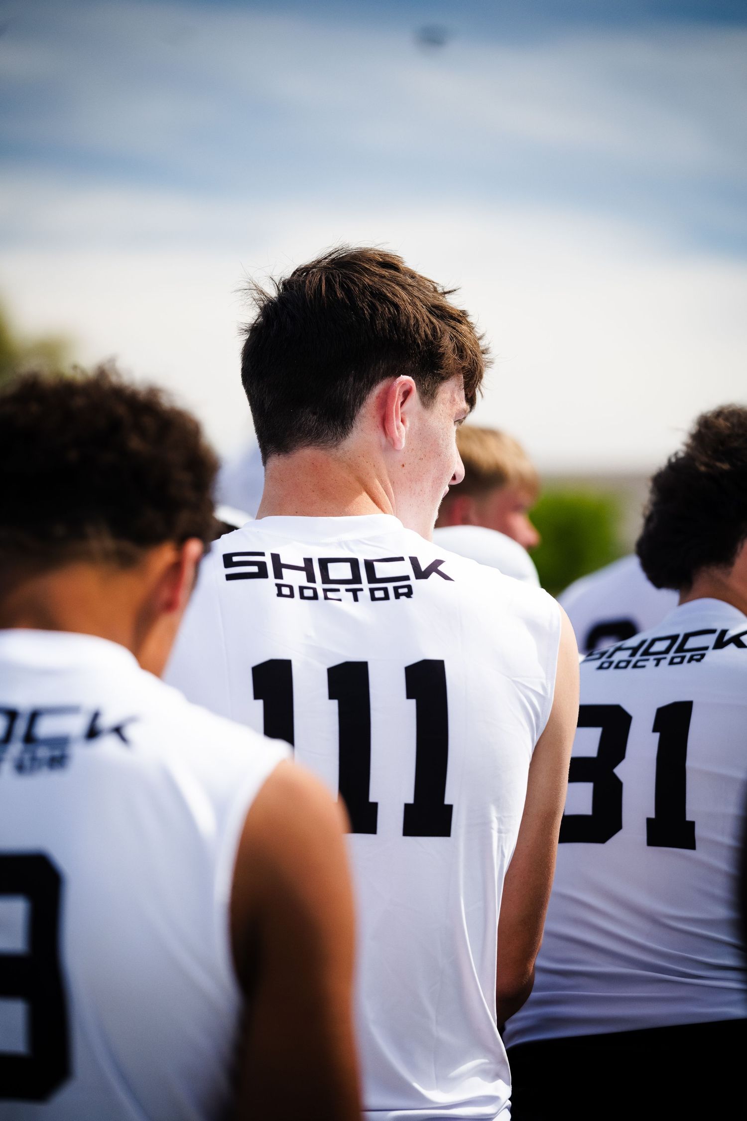 Athletes wearing Shock Doctor jerseys including number 111 stand together at an outdoor football camp.