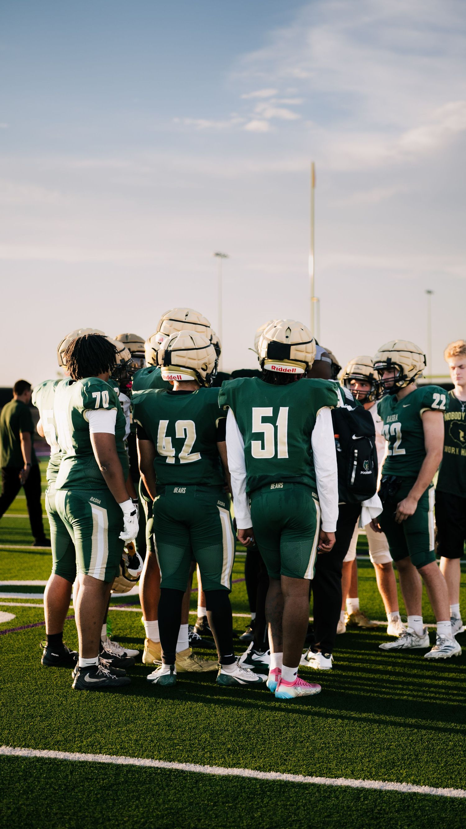High school football players in green uniforms huddle together on the field before a game.