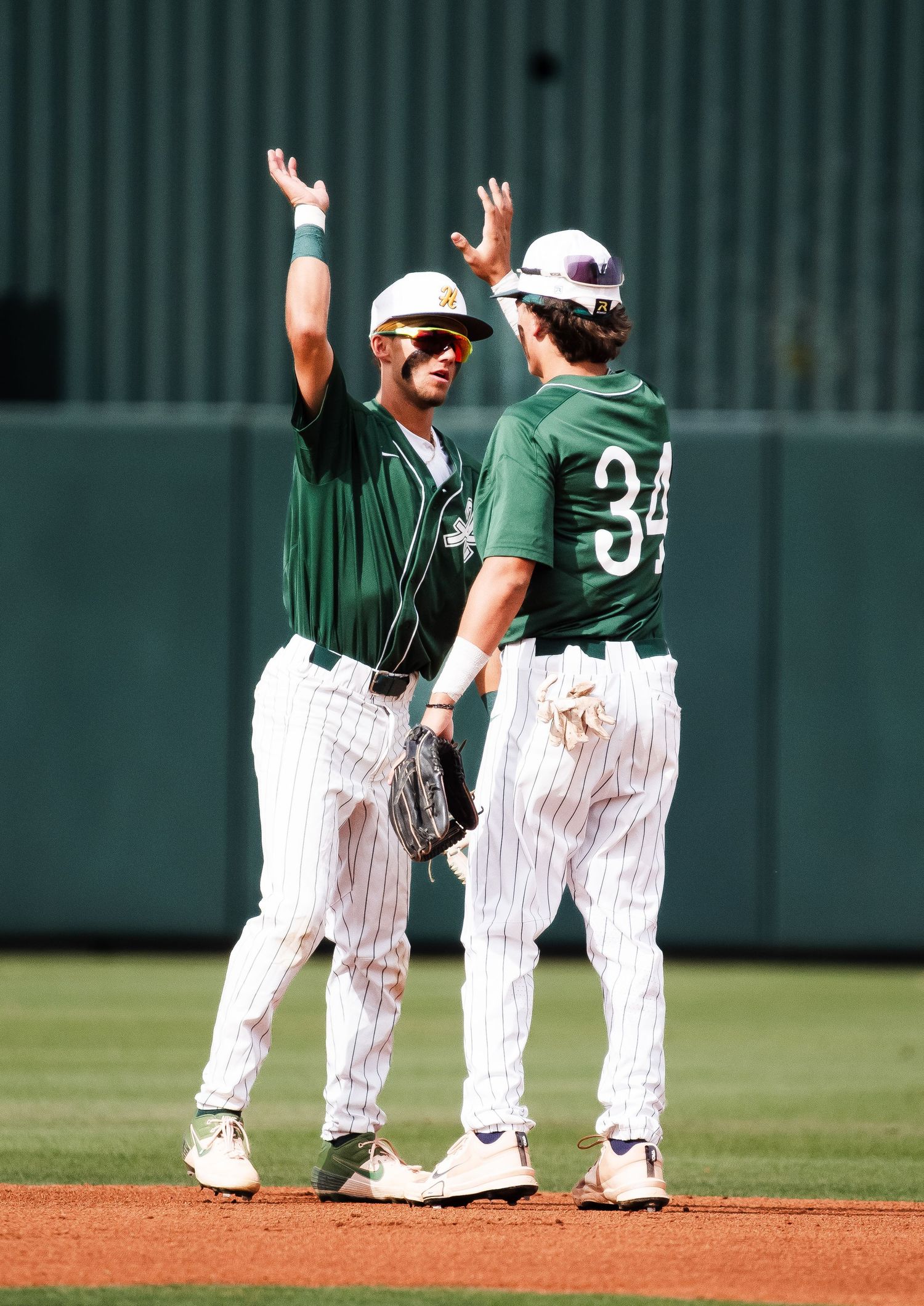 Two baseball players in green uniforms high-fiving on field.