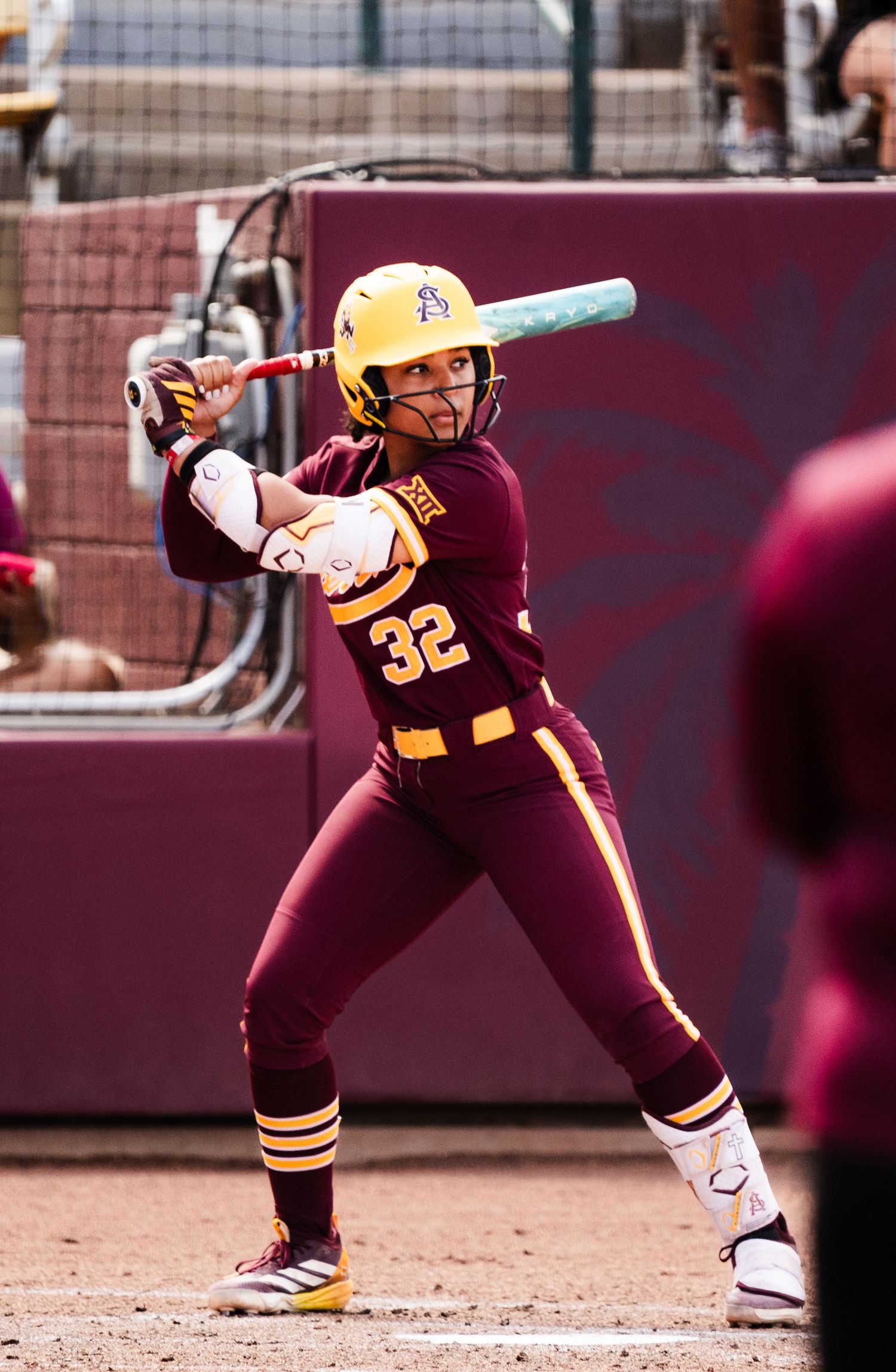 Arizona State Sun Devils softball player #32 in maroon uniform stands ready to bat during a college softball game.