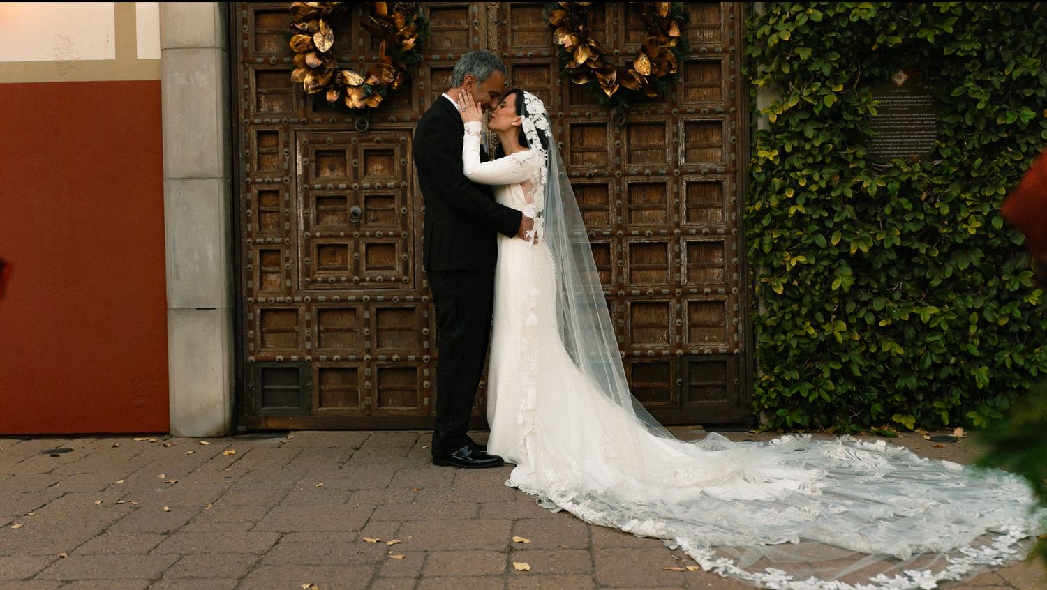 Bride and groom sharing romantic kiss hidden beneath flowing white wedding veil outdoors.