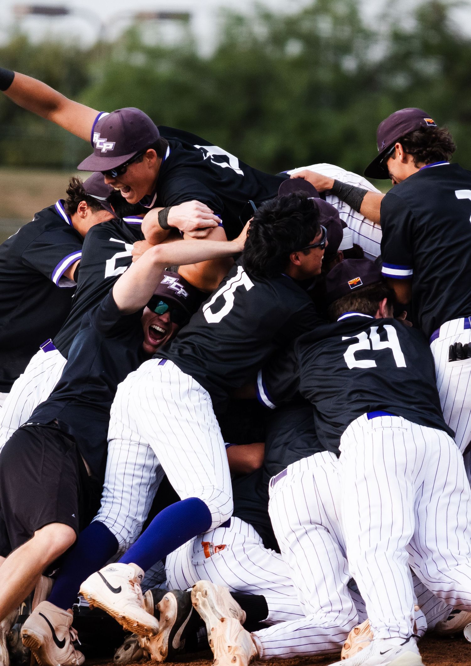 Youth baseball team in black pinstripe uniforms celebrates championship victory in jubilant team pile on field.