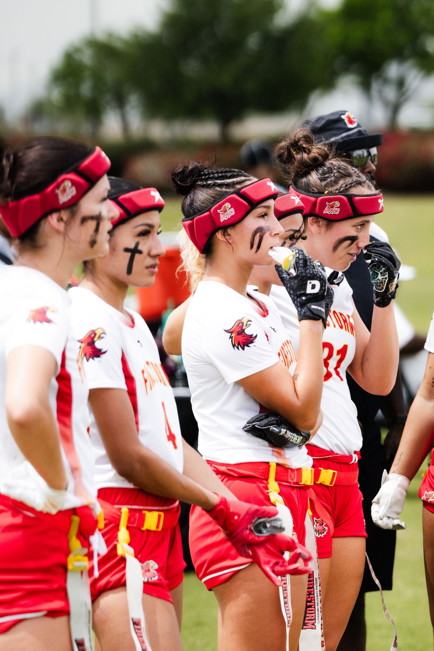 Women's lacrosse team in red and white uniforms line up on field with eye black and red headbands.