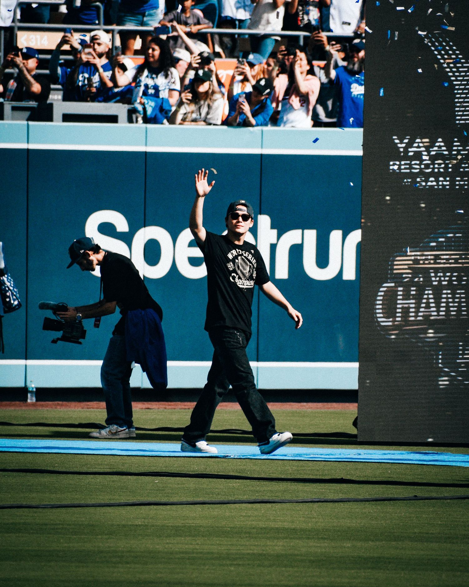 Man waving to crowd at Dodger Stadium near Spectrum sign during World Champions celebration event.