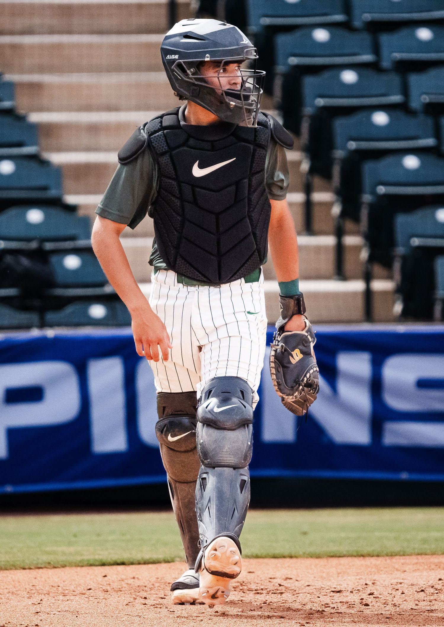 Baseball catcher in full Nike gear walking on field during game.