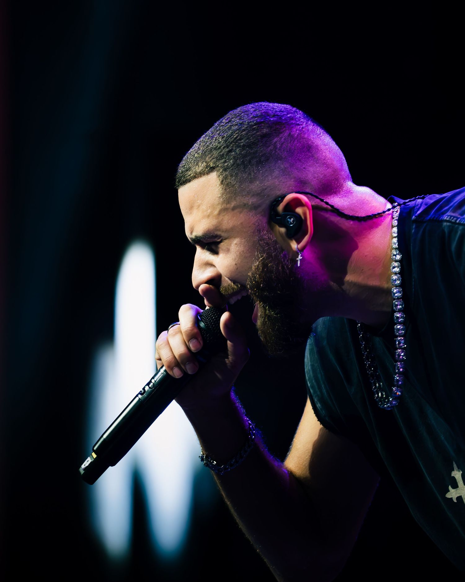Male performer singing passionately into microphone on stage under purple and blue concert lighting.