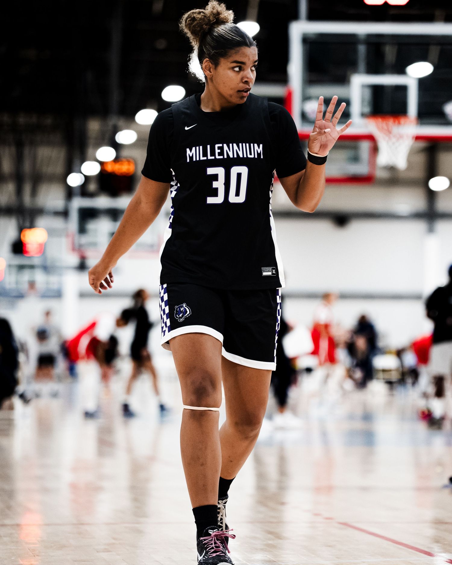 Female basketball player #30 in black Millennium uniform signals on indoor basketball court during a game.
