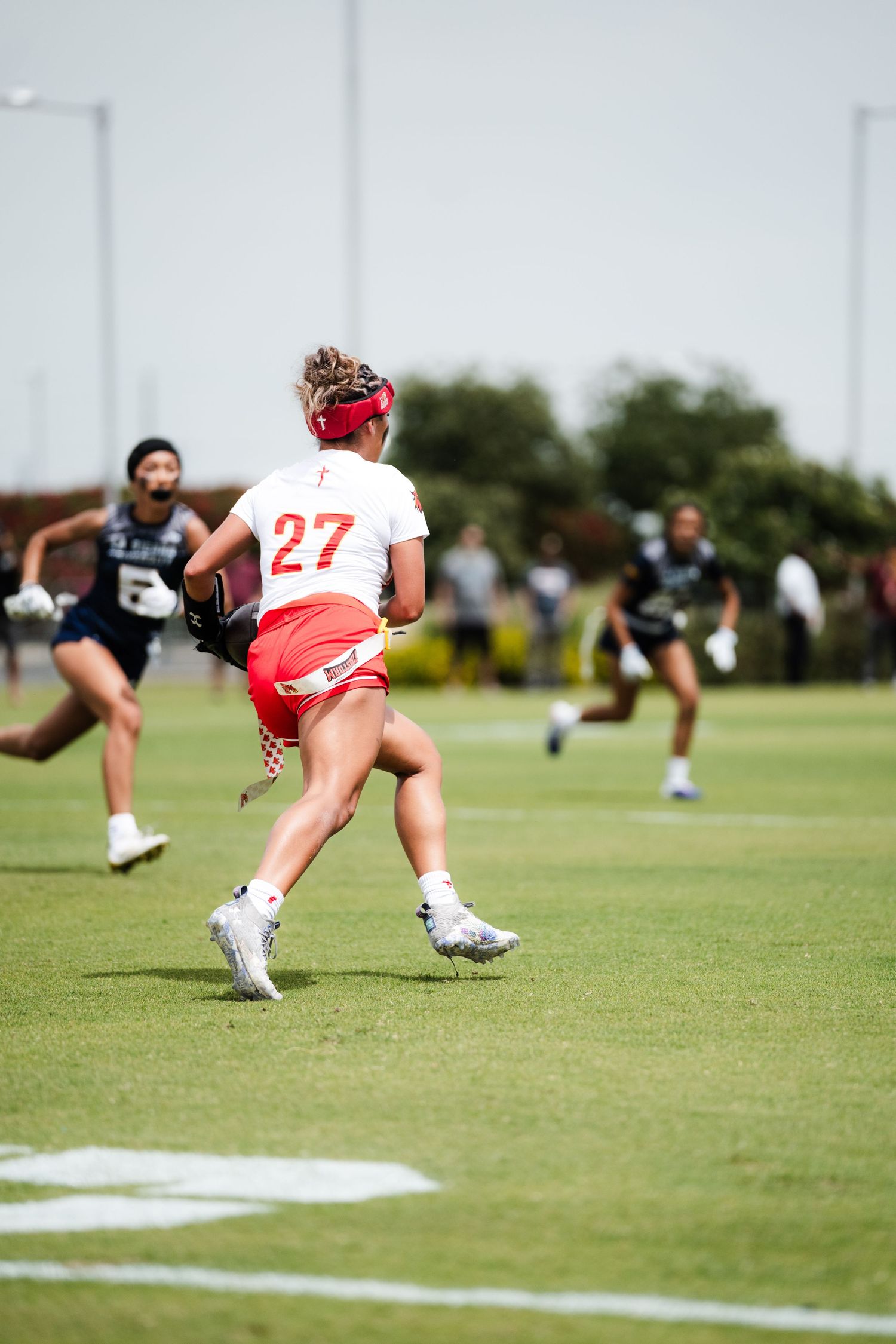Female lacrosse player #27 in red and white Firestorm uniform sprinting with ball during outdoor game.