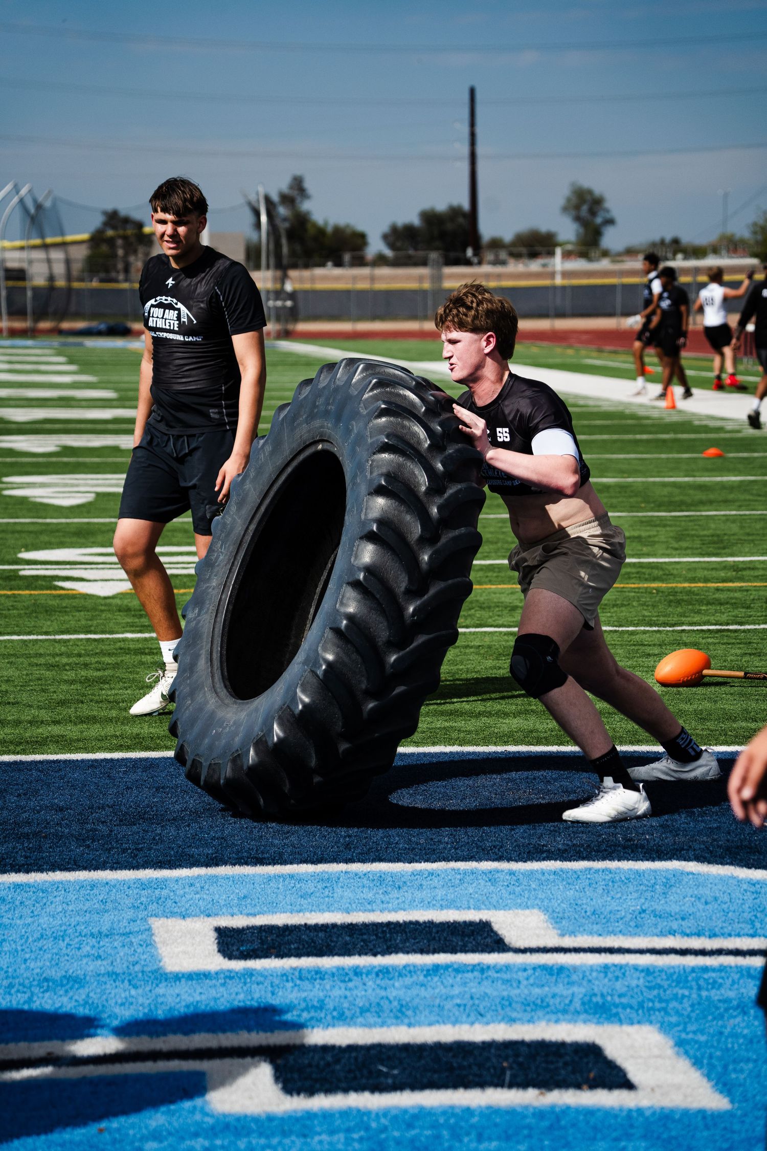 Football player flipping large tractor tire during strength training drill on blue turf field.