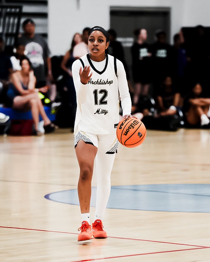 Female basketball player #12 in Archbishop Mitty uniform dribbles ball on indoor court during game.