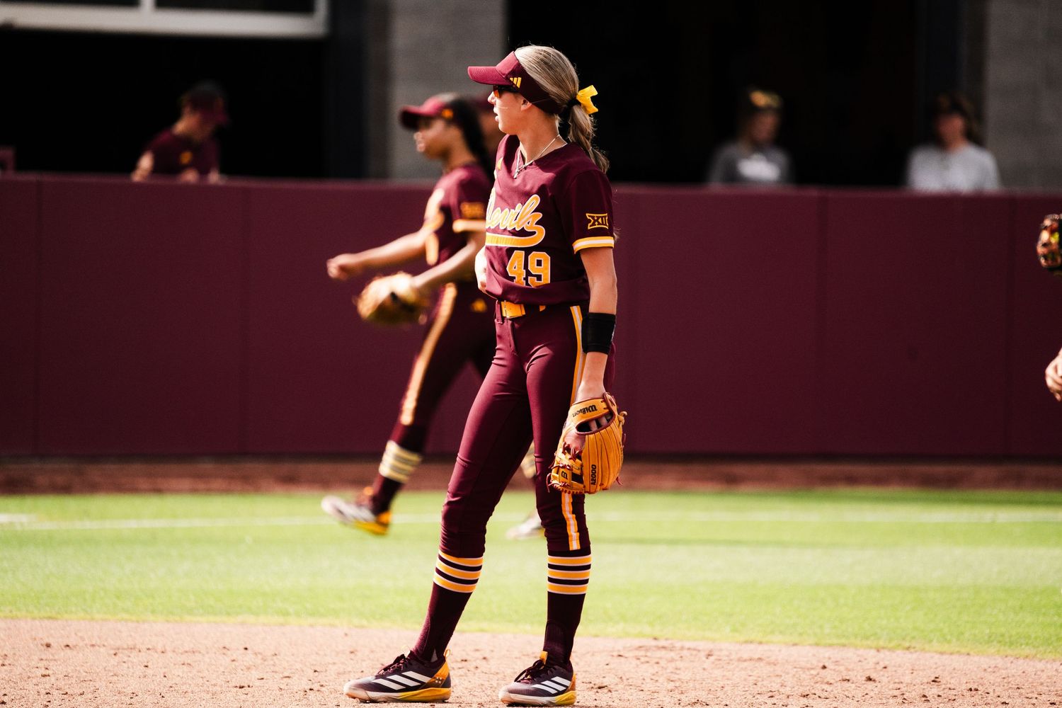 ASU softball player number 49 in maroon and gold uniform stands on field during a college softball game.