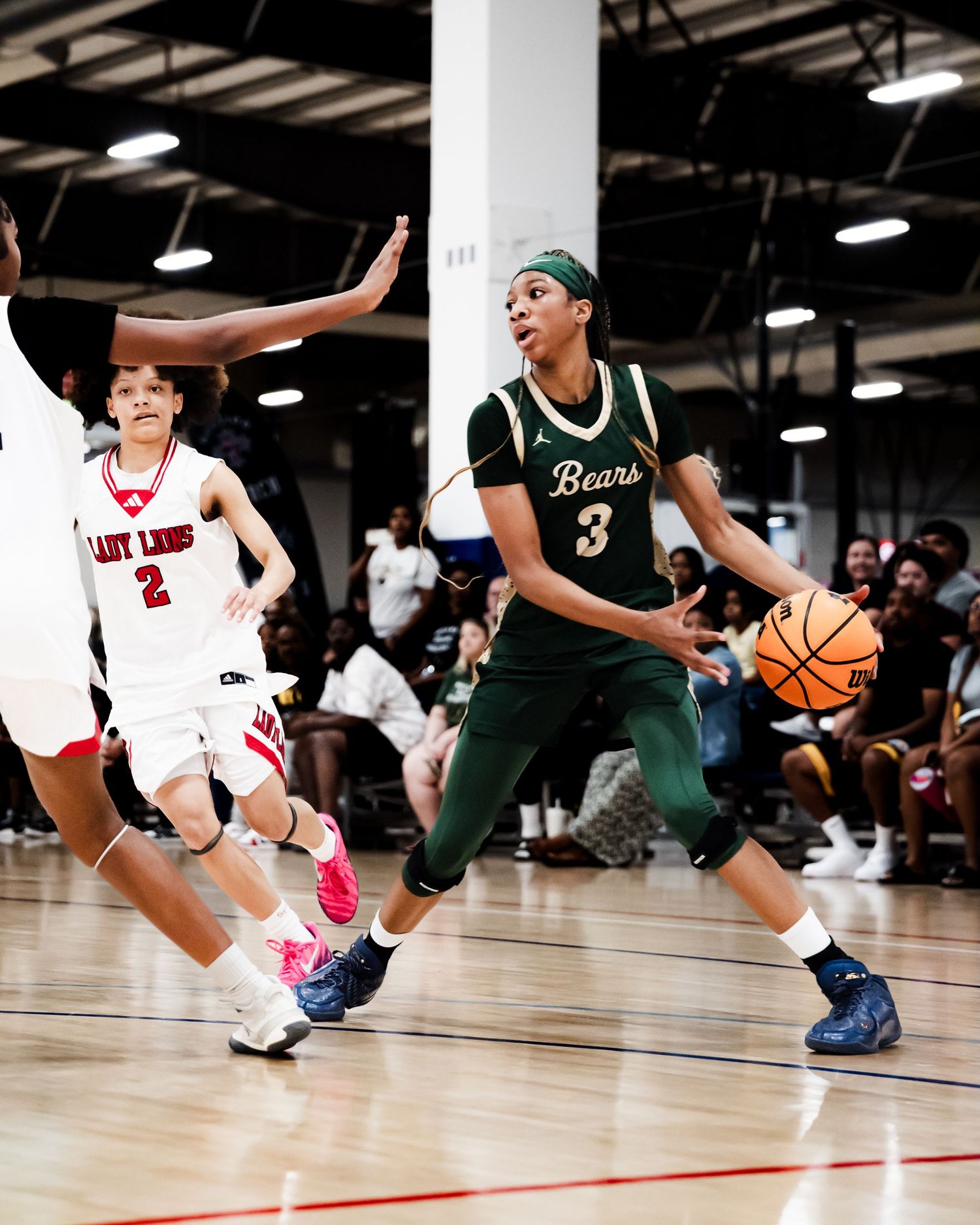 Female basketball player #3 in green Bears uniform drives to basket during competitive game.