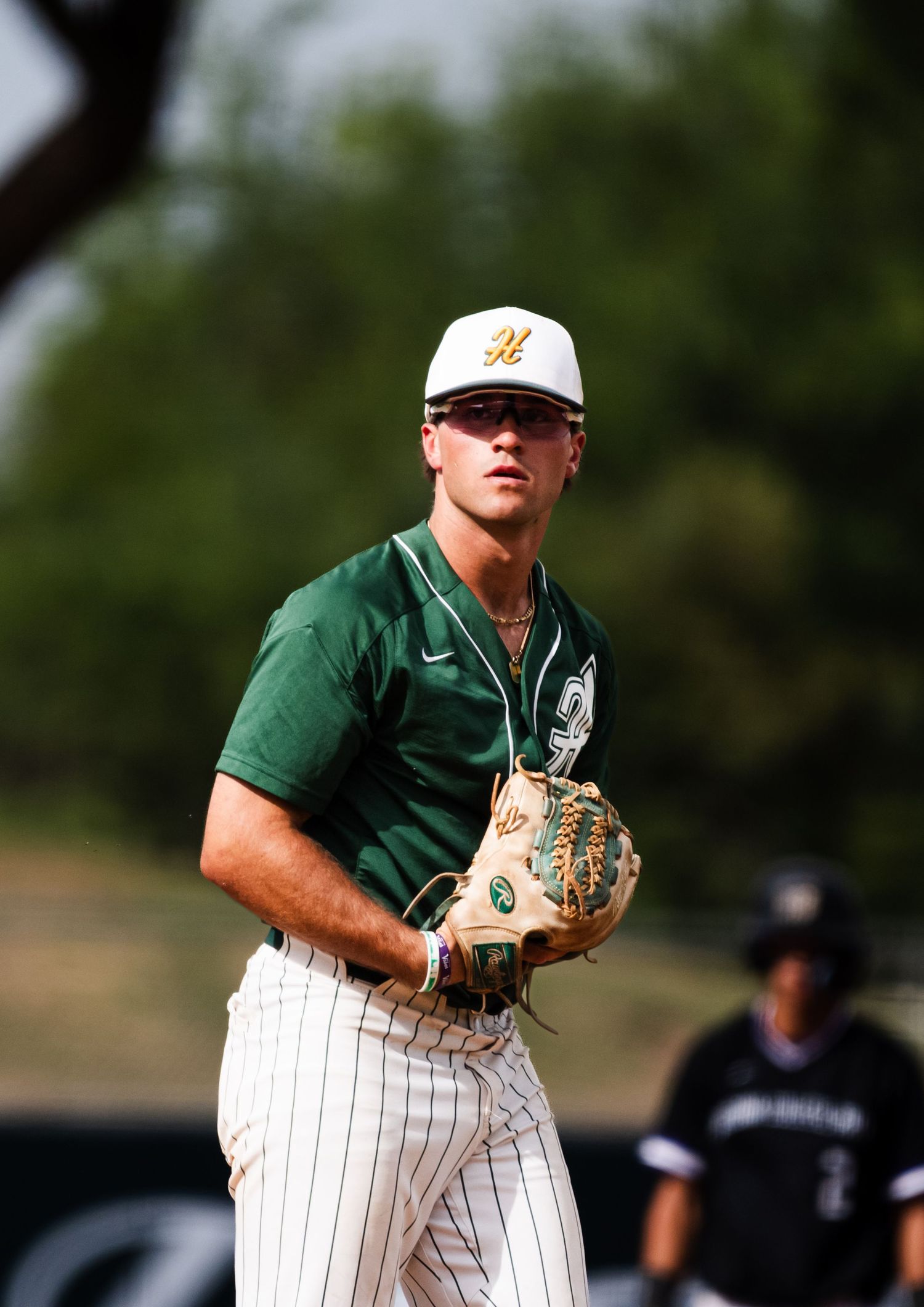 Baseball pitcher in green Nike uniform holding glove on field during game.