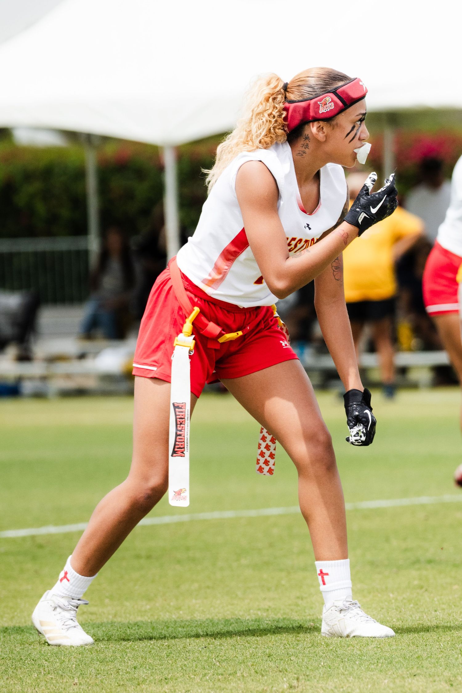 Female flag football player in red shorts and white jersey in athletic stance during an outdoor game.