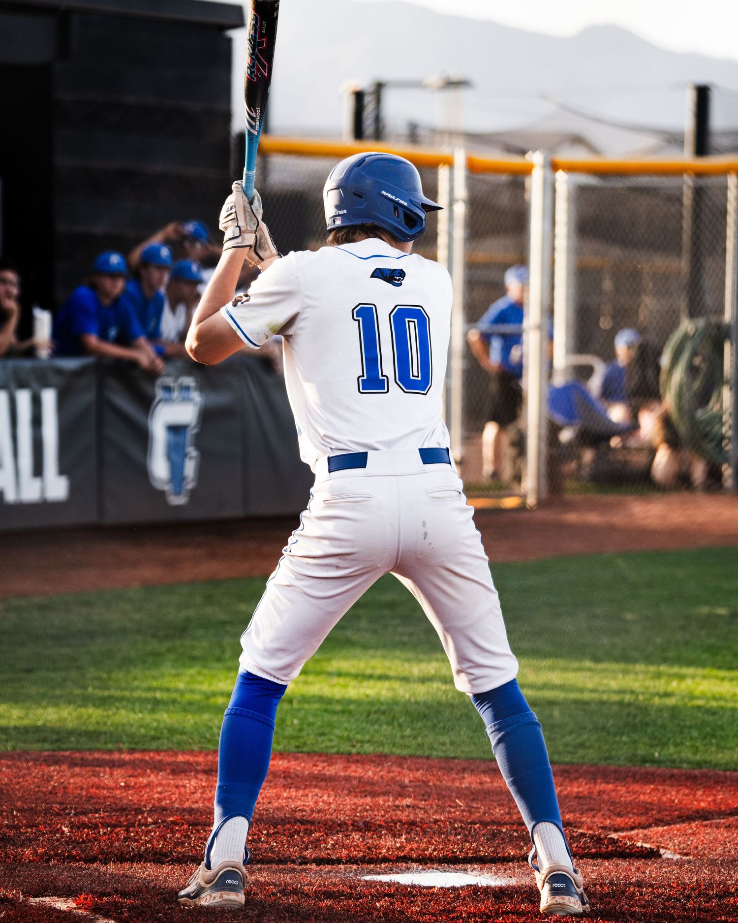 Baseball player number 10 in white uniform stands at bat during a game, wearing a blue helmet.