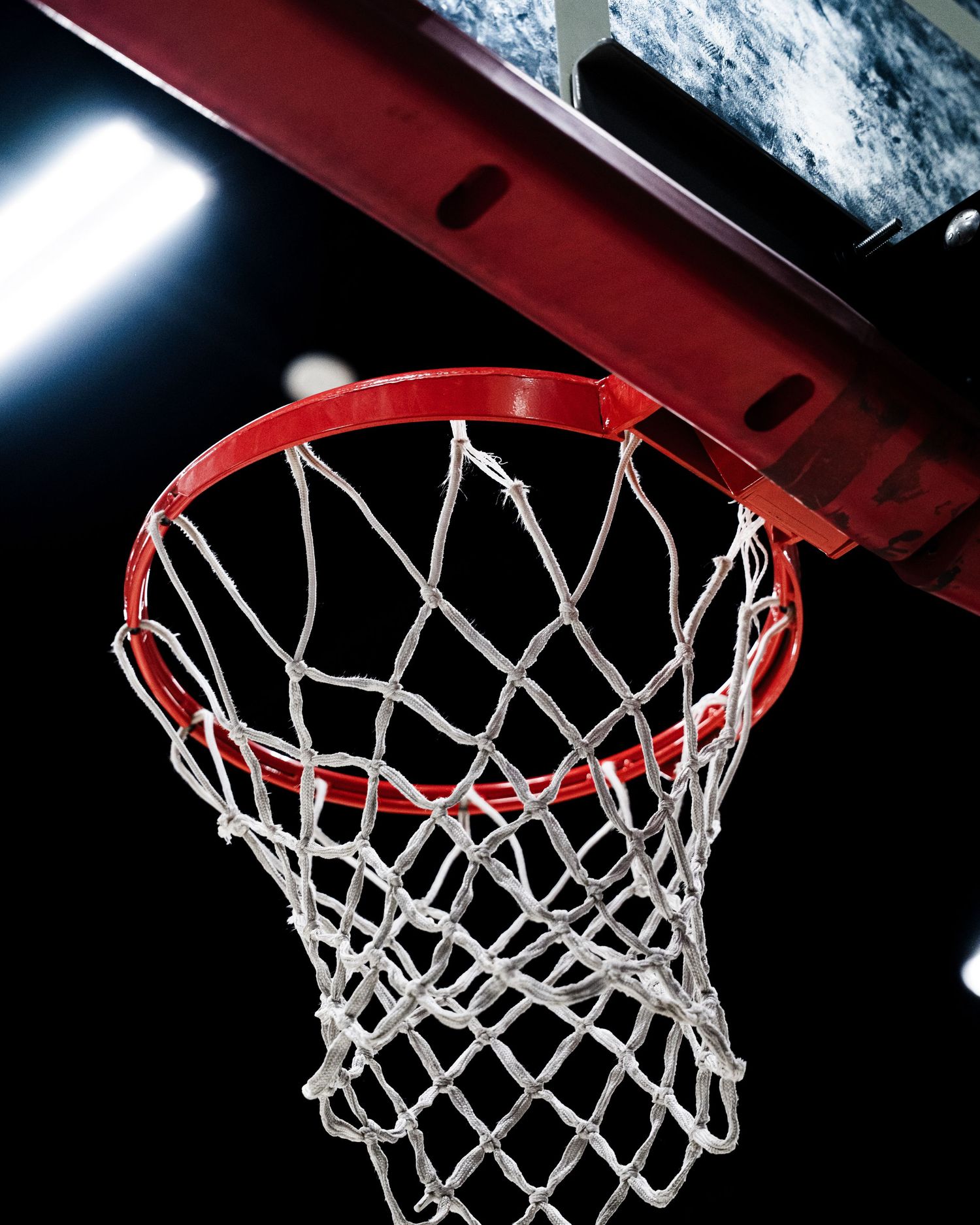 Low angle view of a red basketball hoop and white net against a dark arena background.