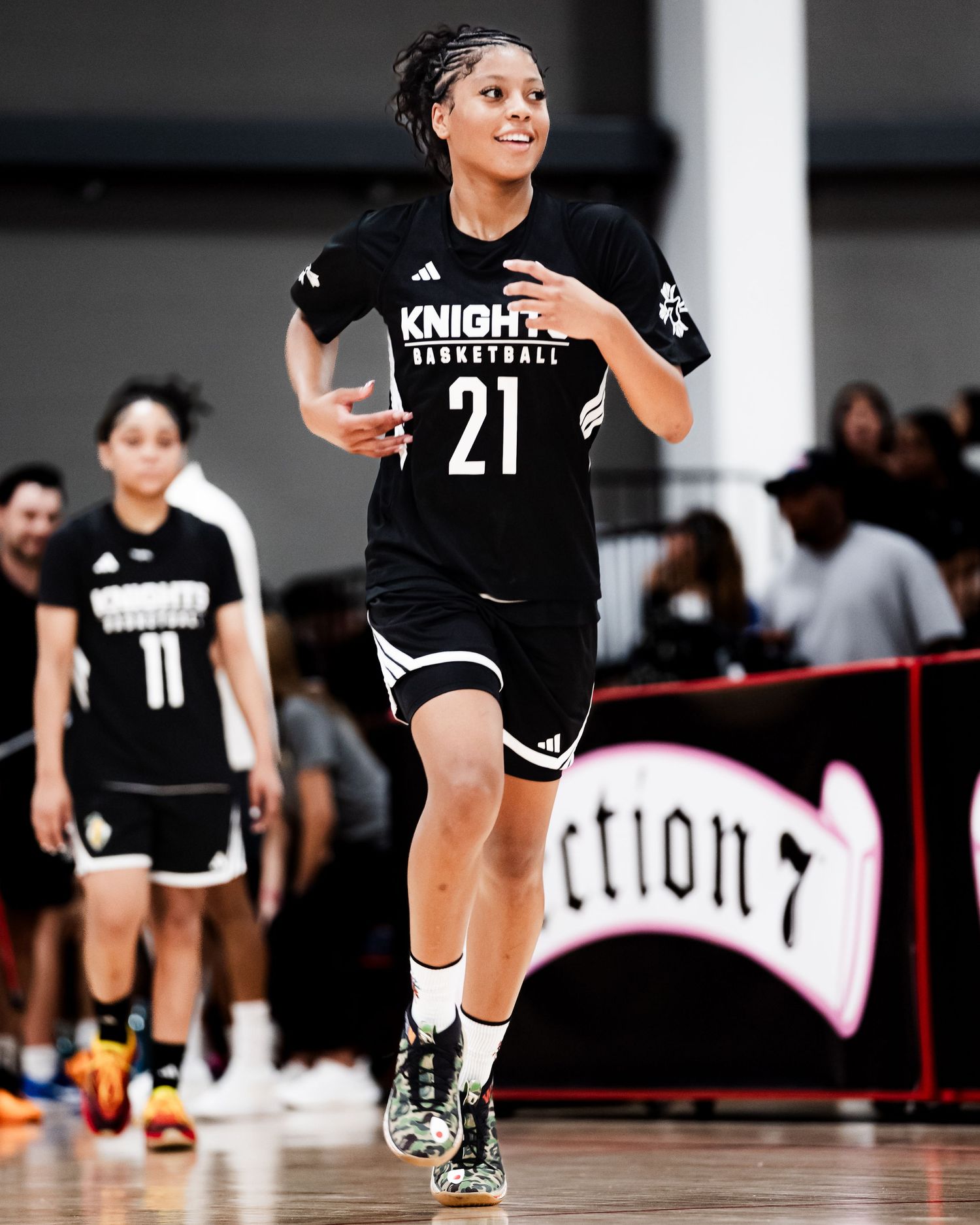 A female basketball player in a black Knights Basketball number 21 jersey runs on an indoor court.