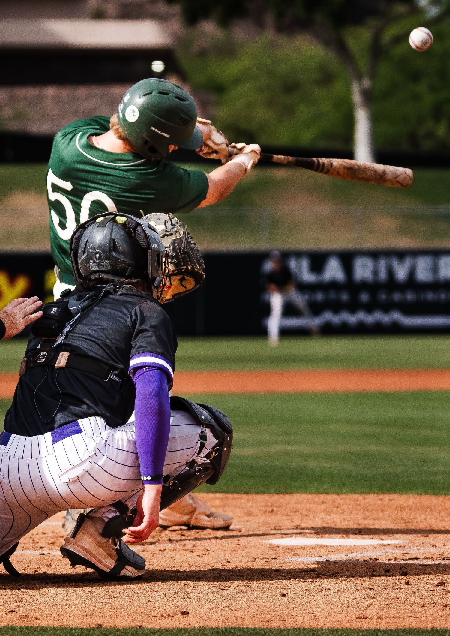 Baseball batter in green jersey number 50 swings at pitch while catcher crouches behind home plate during game.