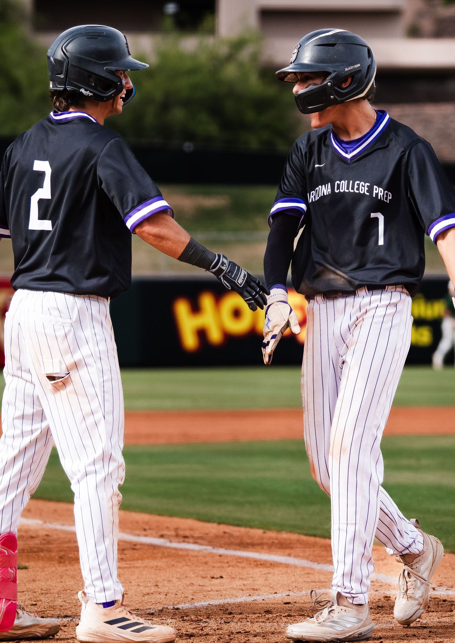 Two Arizona College Prep baseball players #2 and #1 celebrate with a handshake on the field.