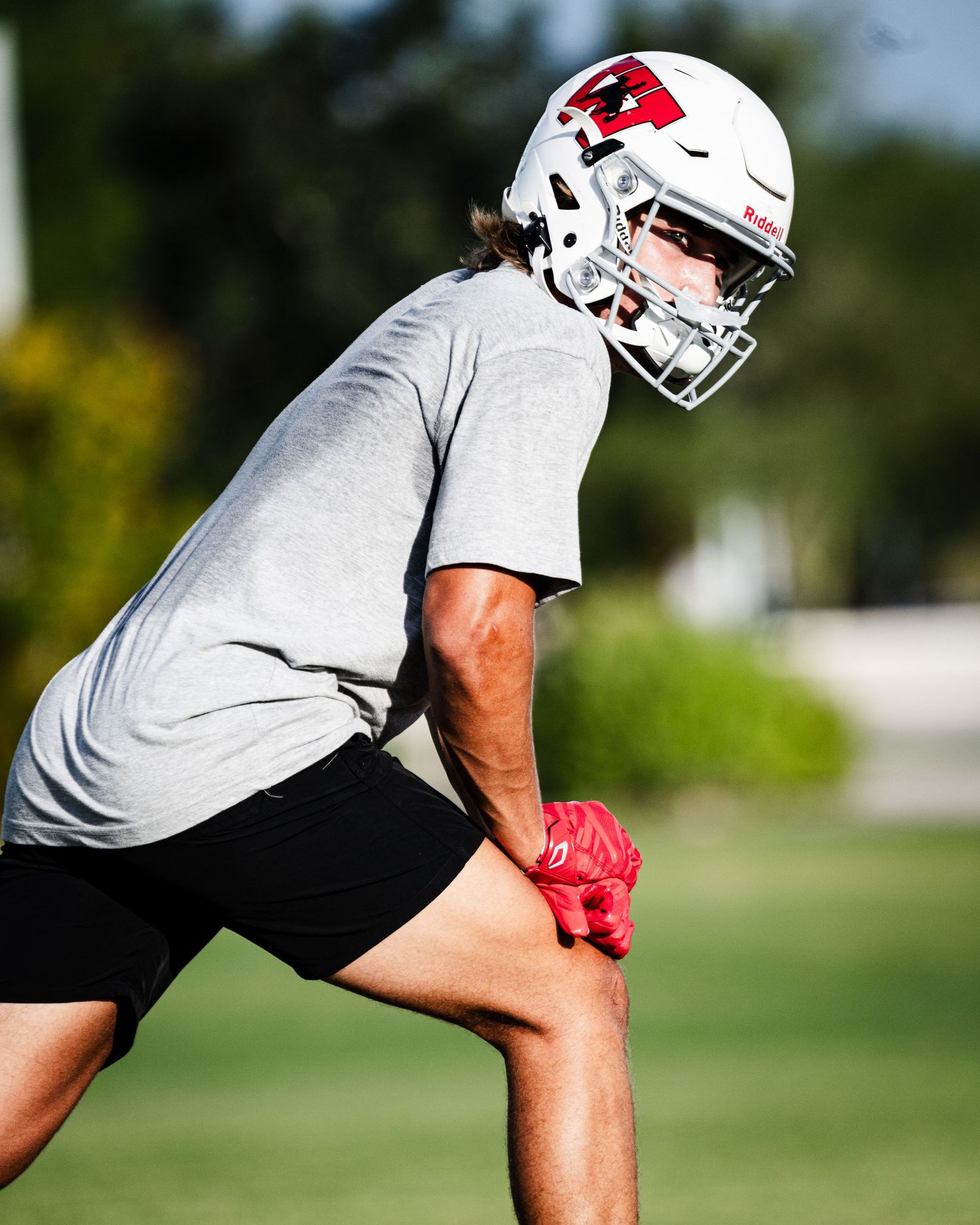 Football player in white helmet and gray shirt stretches on green field during practice.