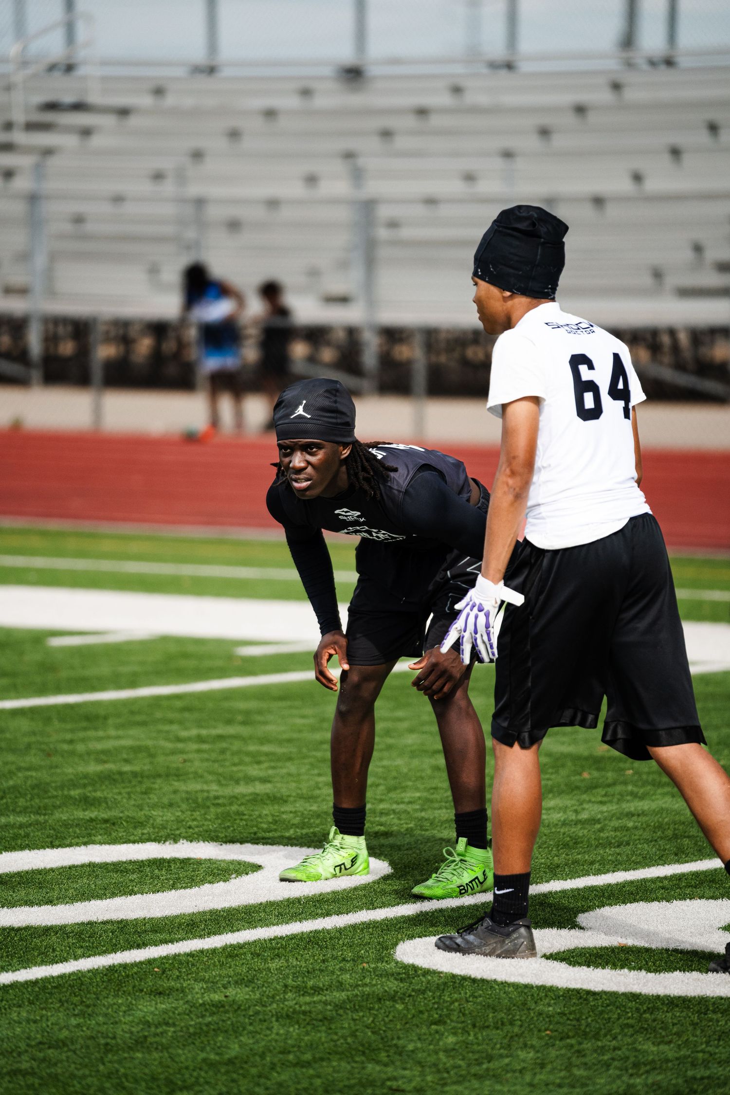 Two football players in black uniforms practice drills on green turf field during training.