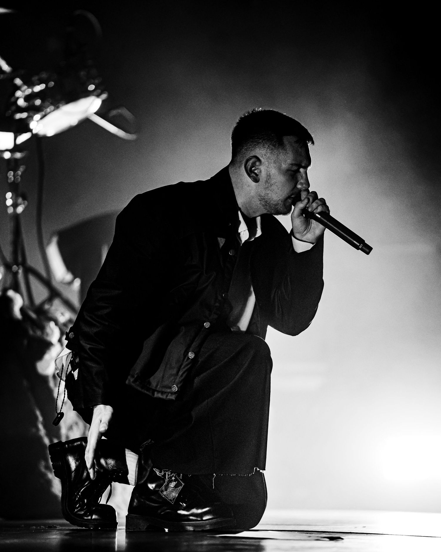 Black and white photo of a male singer kneeling on stage, holding a microphone close to his mouth.