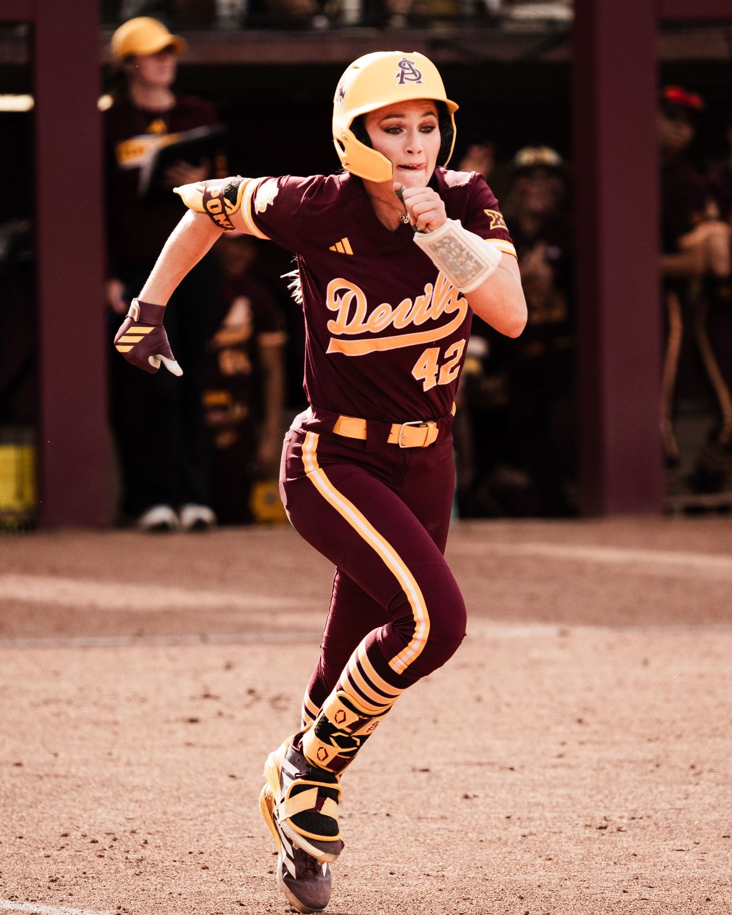 Arizona State Sun Devils softball player #42 sprints in maroon uniform and gold helmet during a night game.