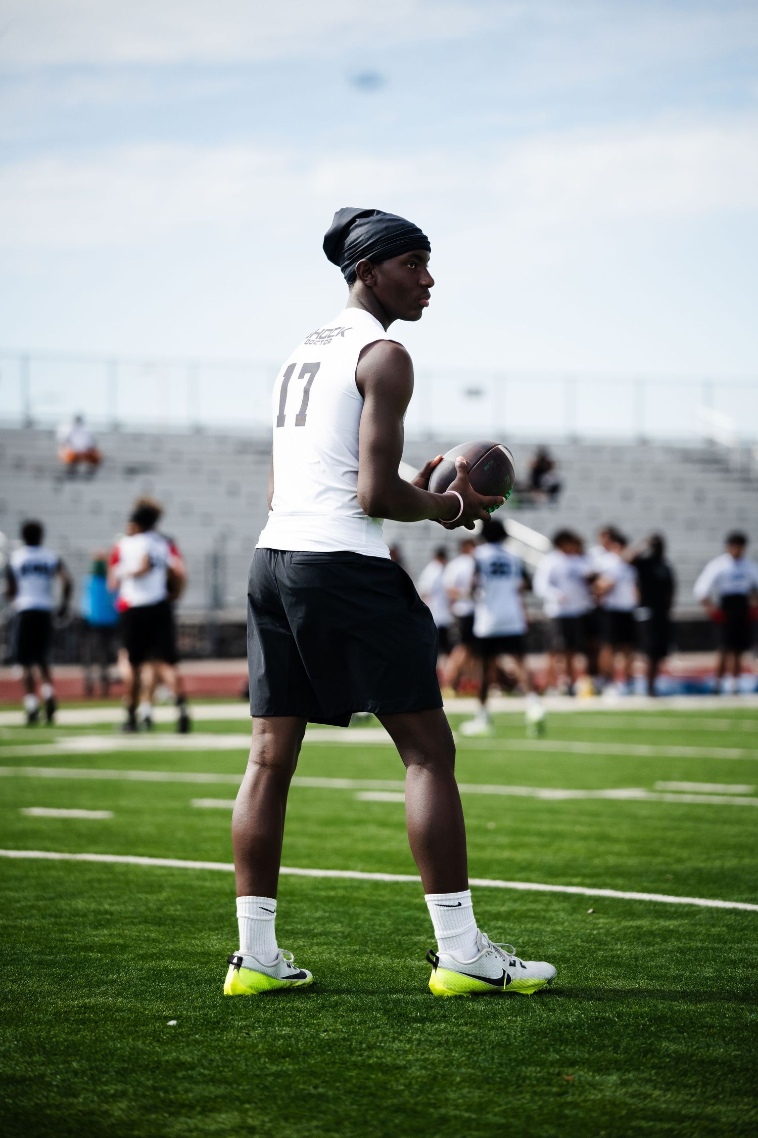 Football player #17 in white jersey holds ball on green field during outdoor practice session.