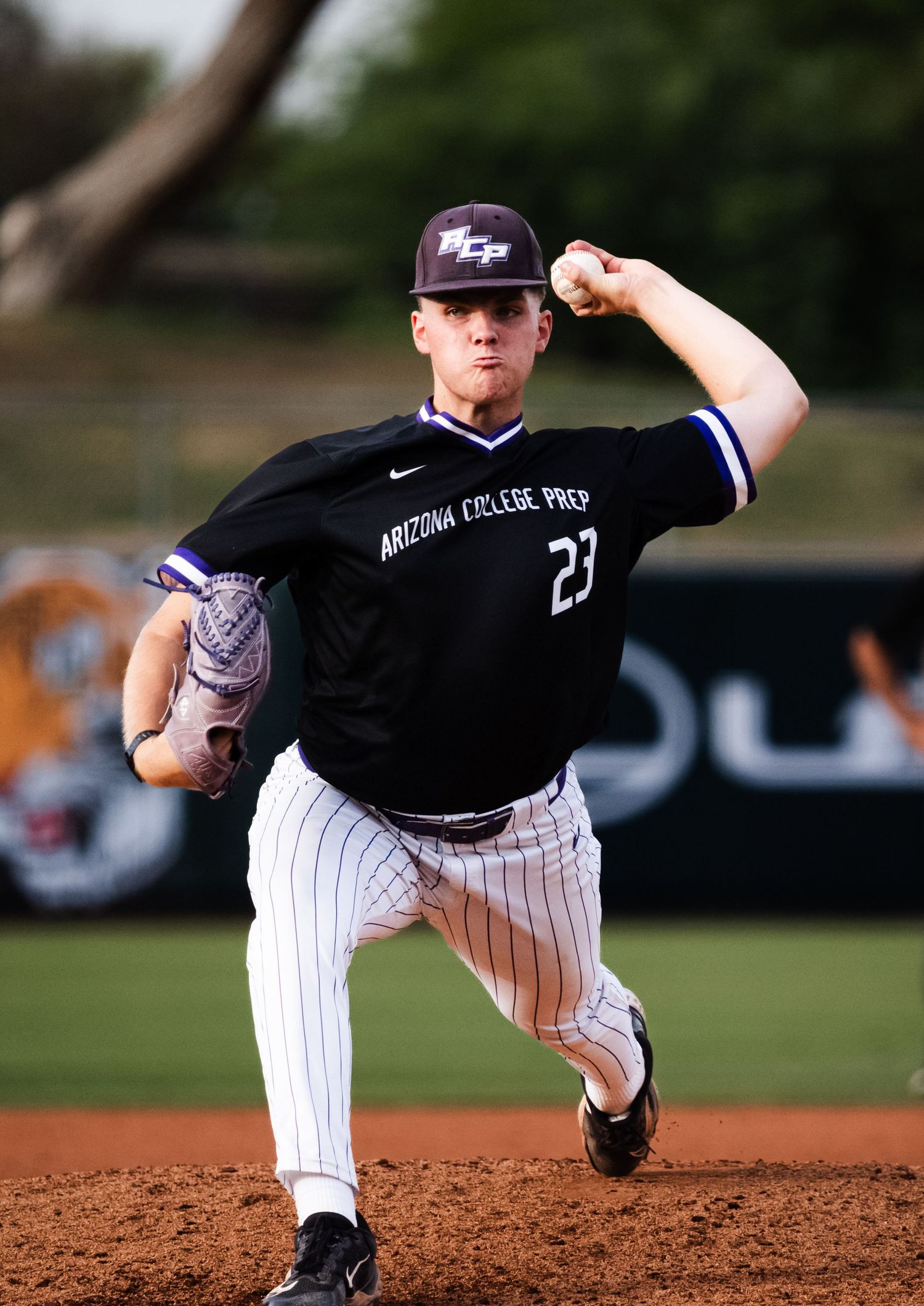 Arizona College Prep baseball pitcher #23 in black pinstripe uniform mid-windup on the mound during a game.