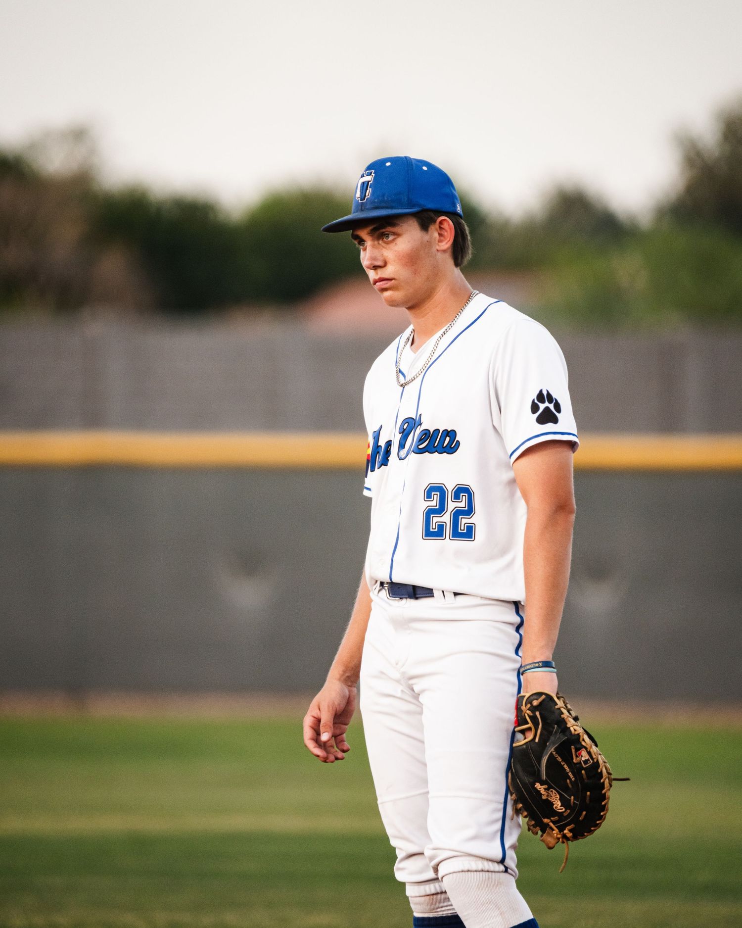 Baseball player #22 in blue and white uniform wearing mitt stands on field during game.
