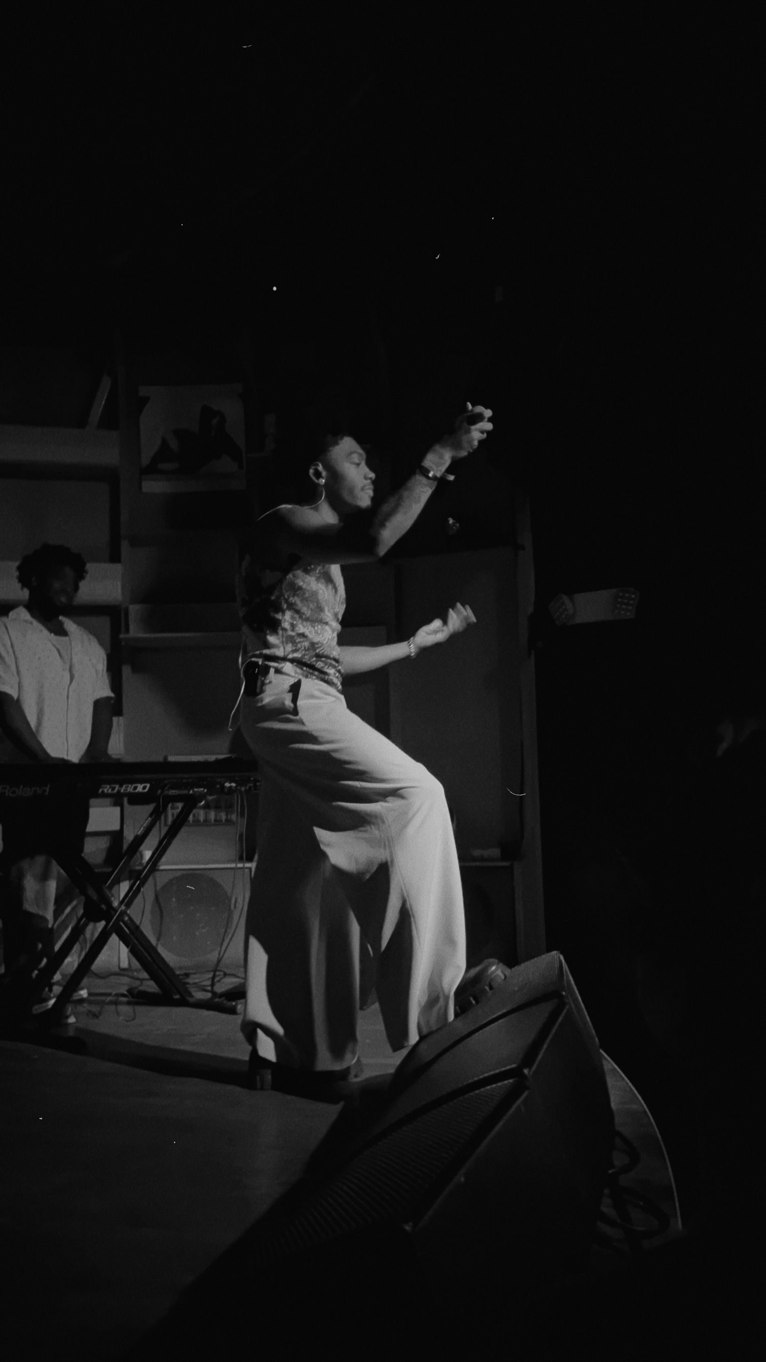 Black and white concert photo of a singer reaching upward on stage with a keyboardist visible behind.