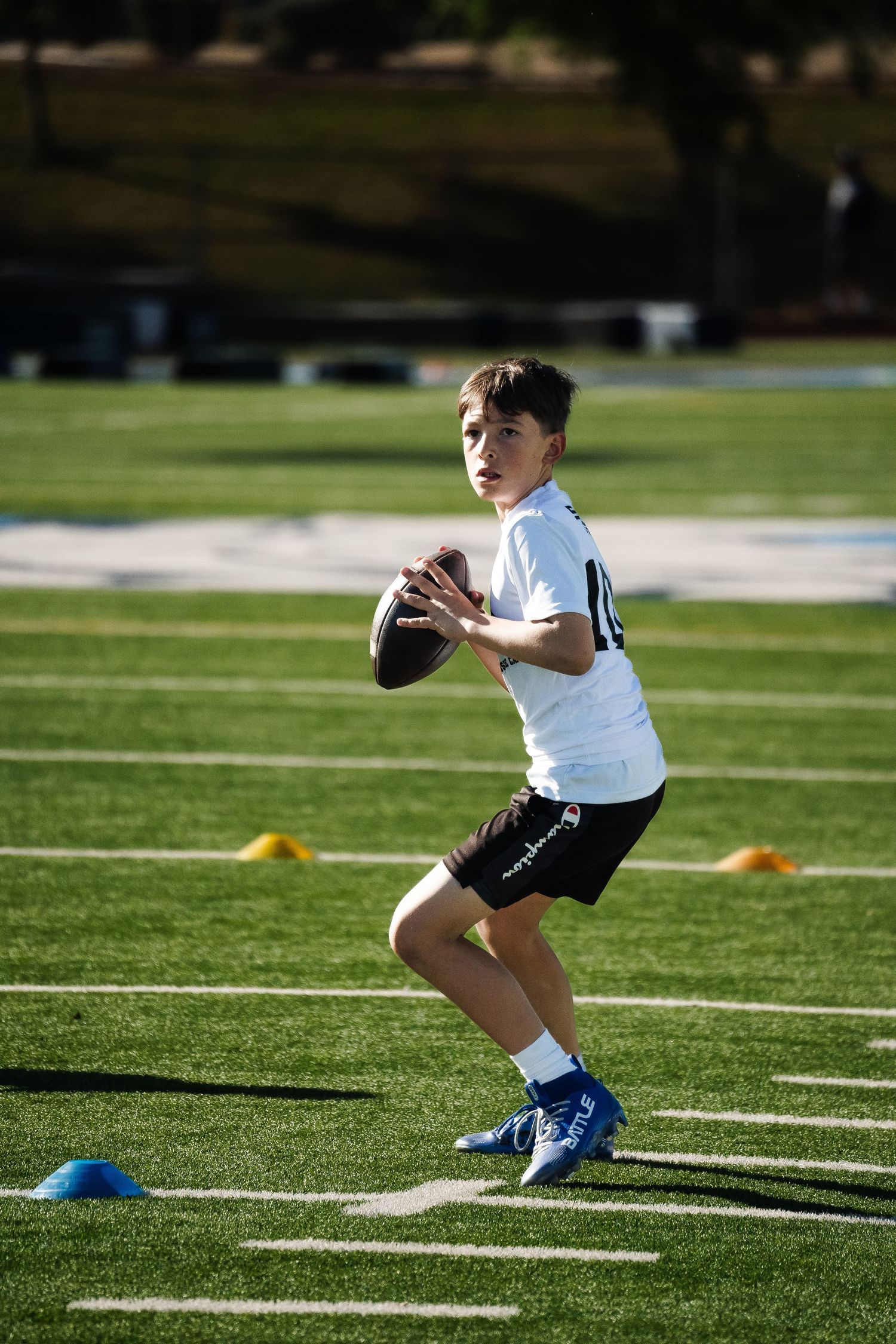 Young quarterback in white jersey preparing to throw football on turf during practice.