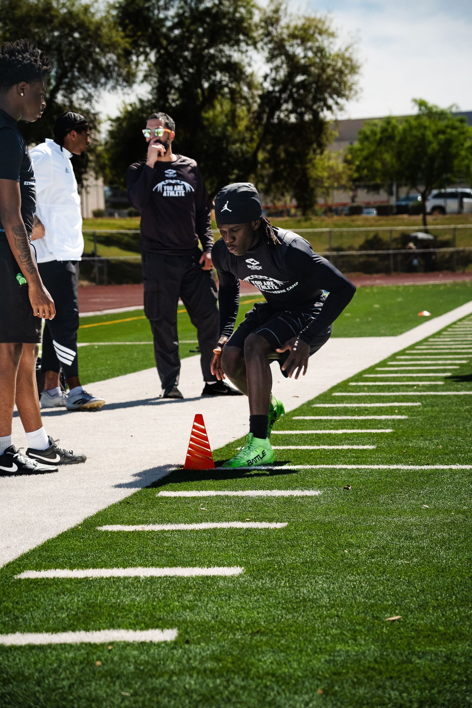Athlete in Jordan gear crouches near orange cone during football agility drill on turf.