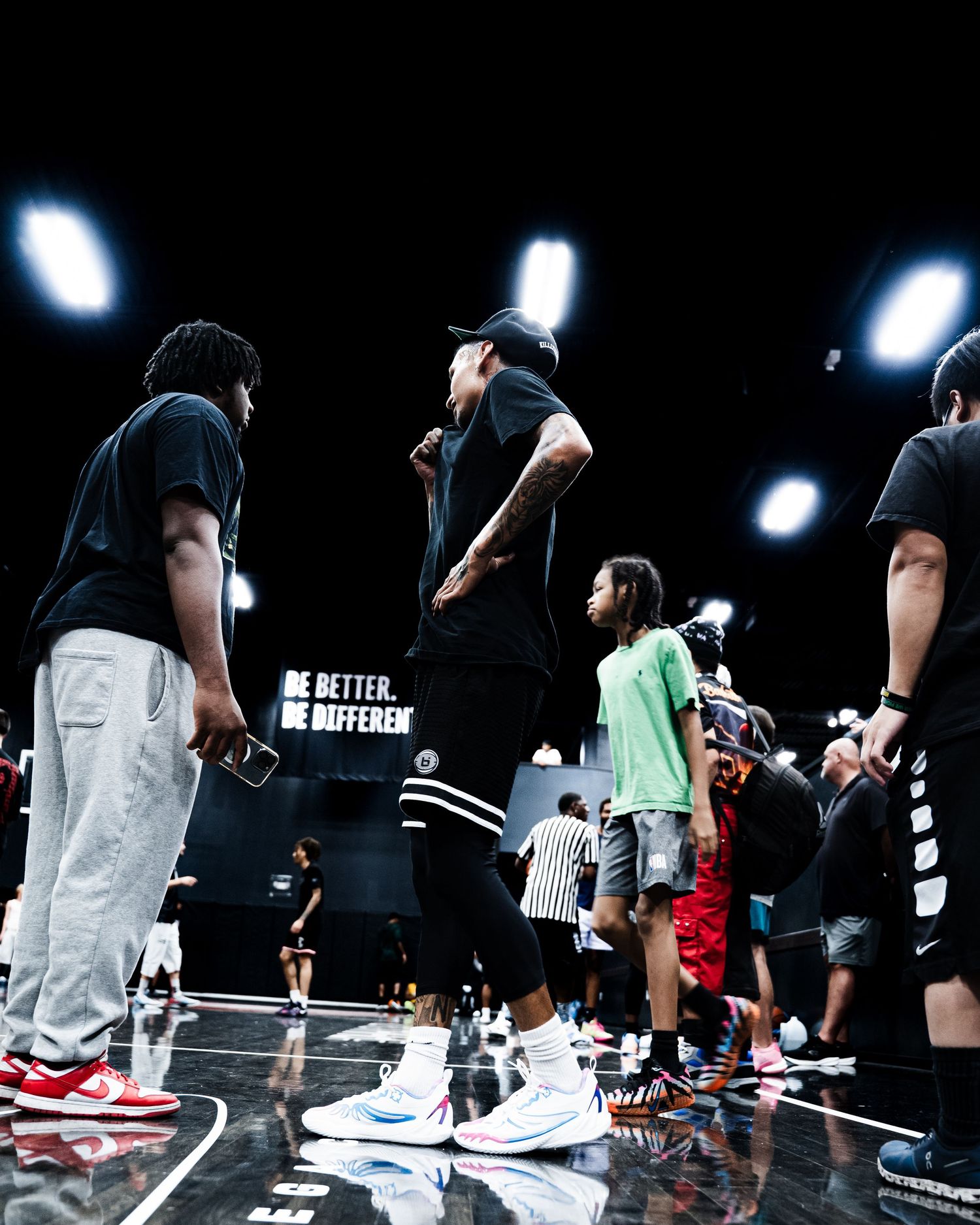 Players and coaches gather on a dark basketball court beneath bright lights at an indoor training event.