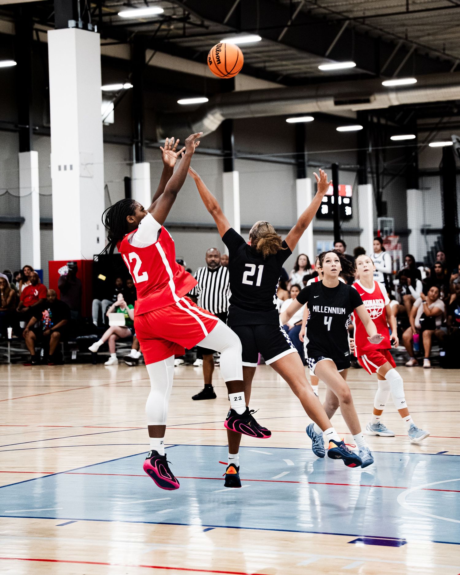Two girls basketball teams battle for a jump ball during a fast-paced indoor high school basketball game.