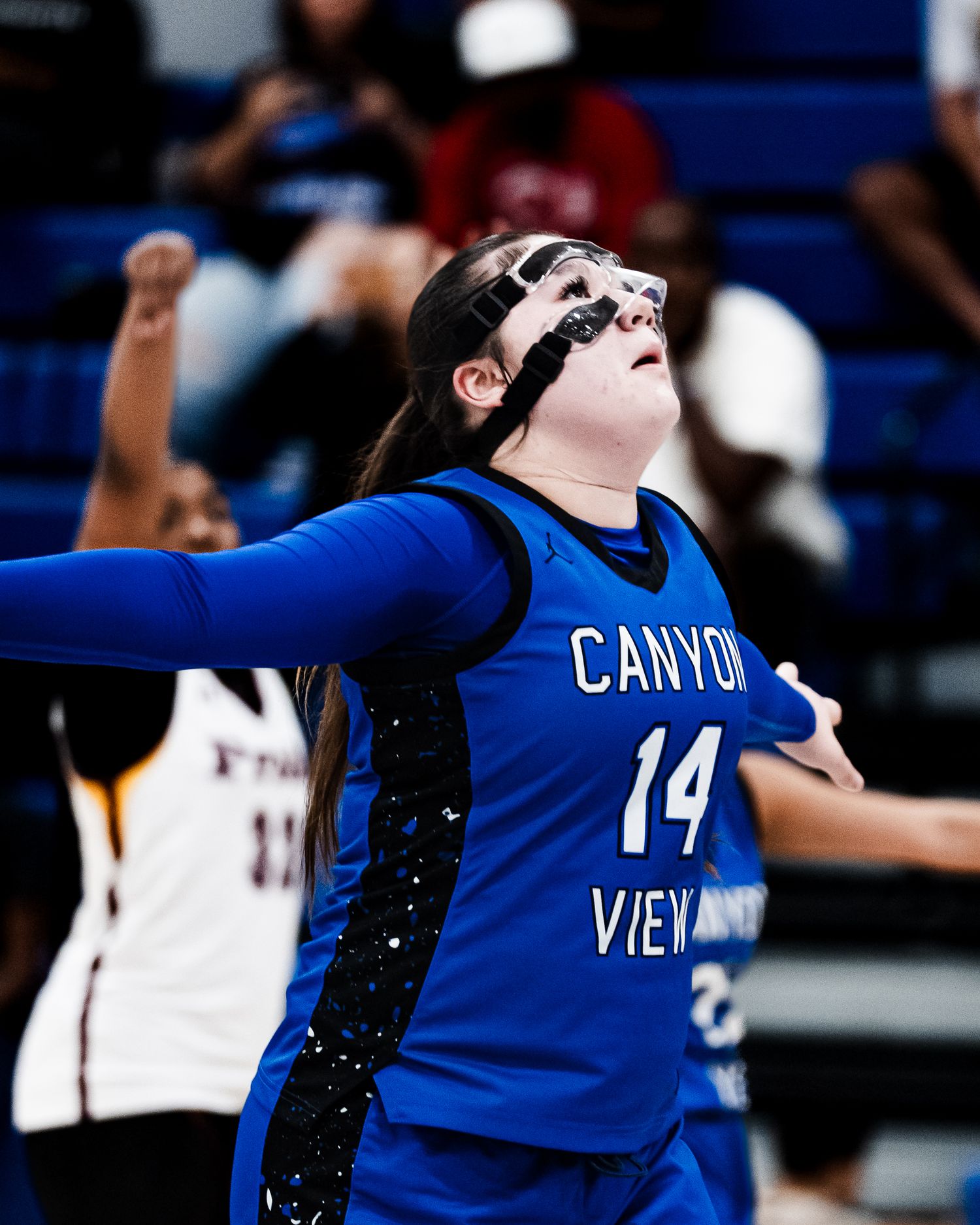 Canyon View #14 female basketball player in blue jersey wearing protective face mask during a game.