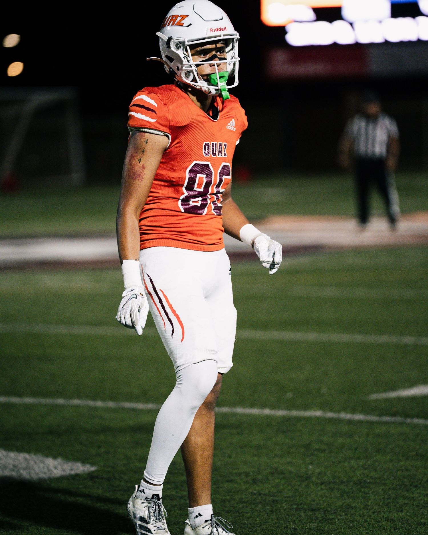 Football player in orange jersey number 86 stands on field at night game wearing white uniform and green mouthguard.