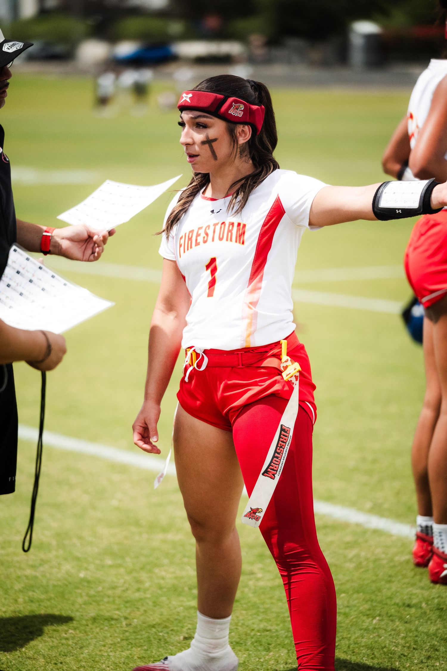 Female flag football player number 1 in Firestorm uniform reviews play sheet on the sideline during a game.