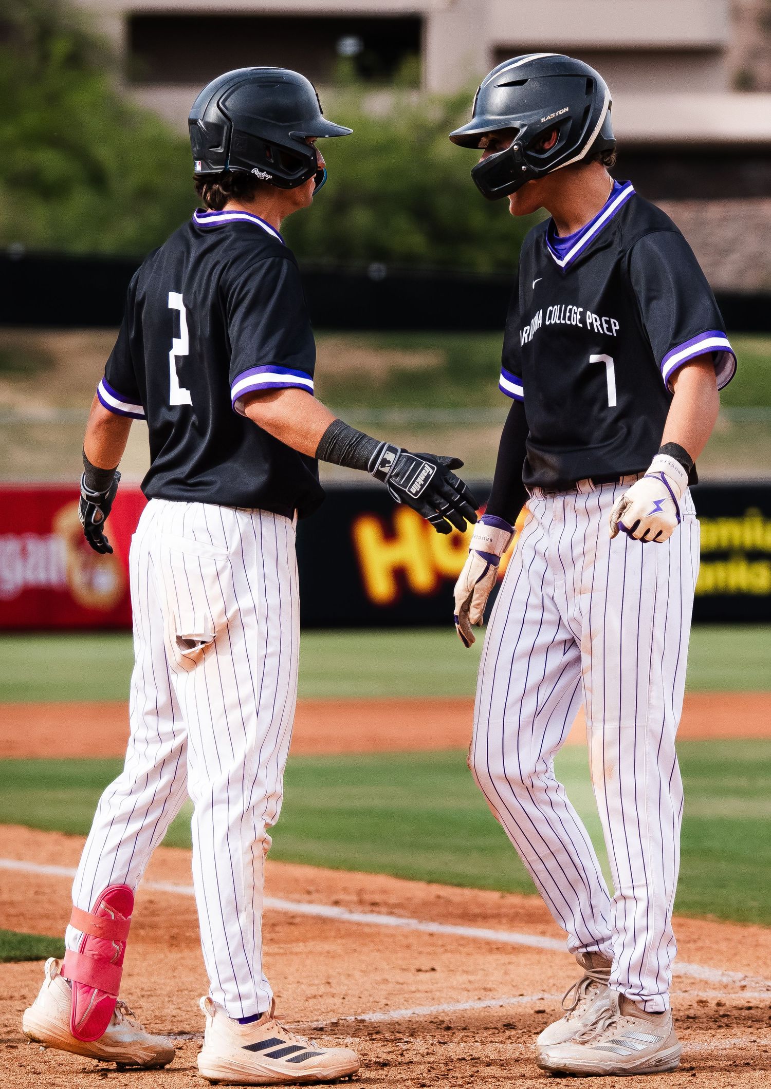 Two Arizona College Prep baseball players in pinstripe uniforms celebrate on the field during a game.