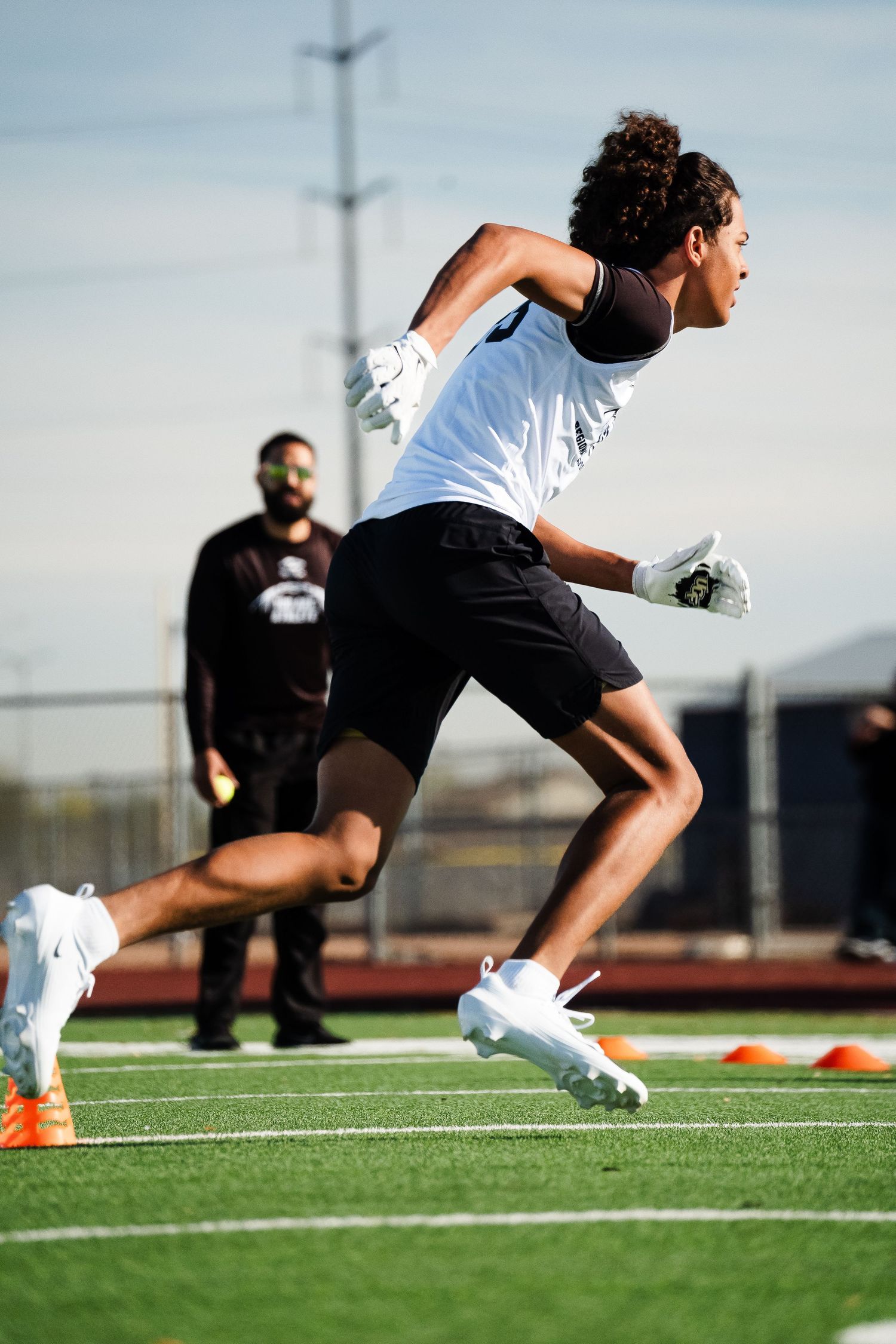Young football player in white uniform accelerating through speed drills on turf field.