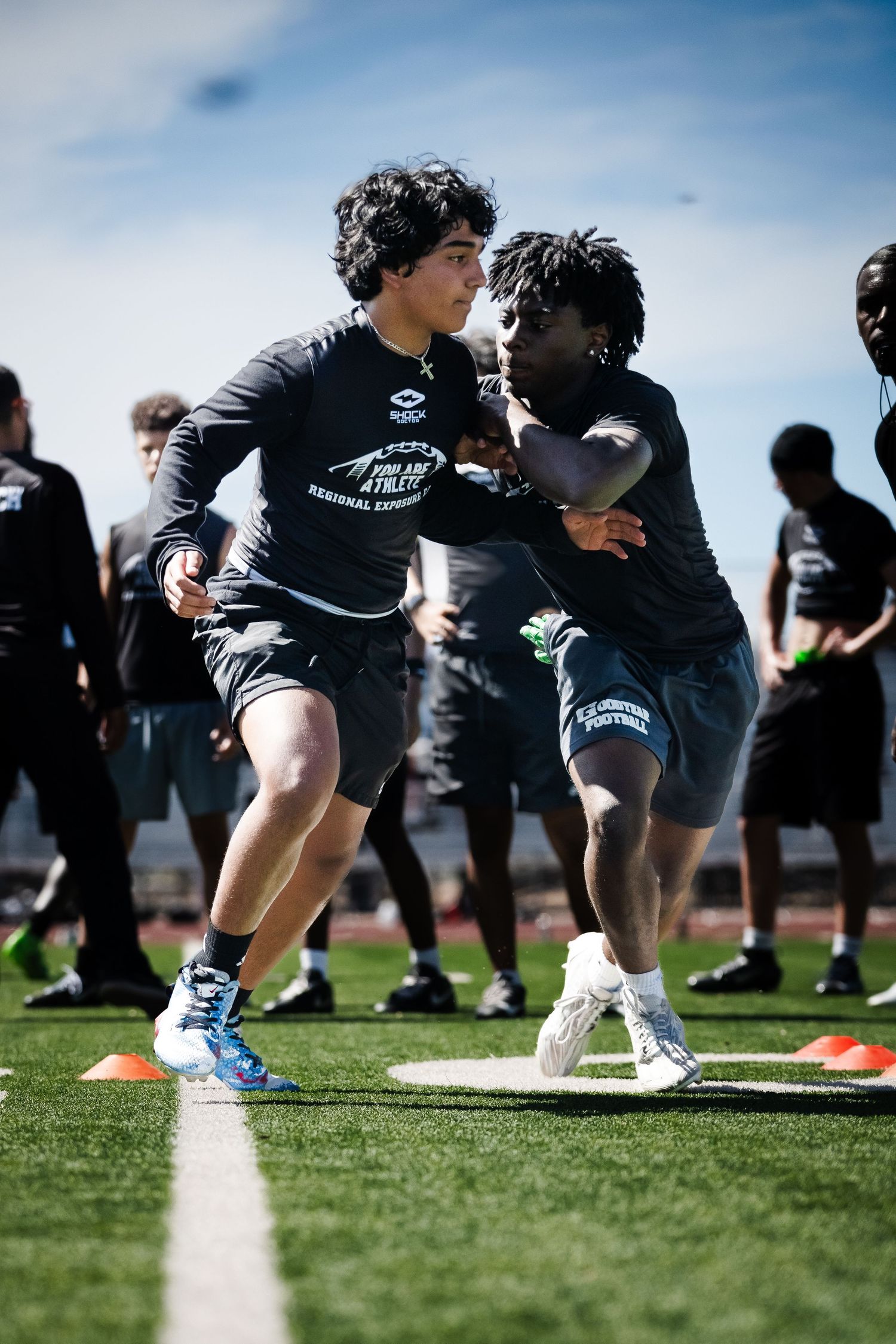 Two football players practice blocking drills at a regional athlete exposure camp on a turf field.