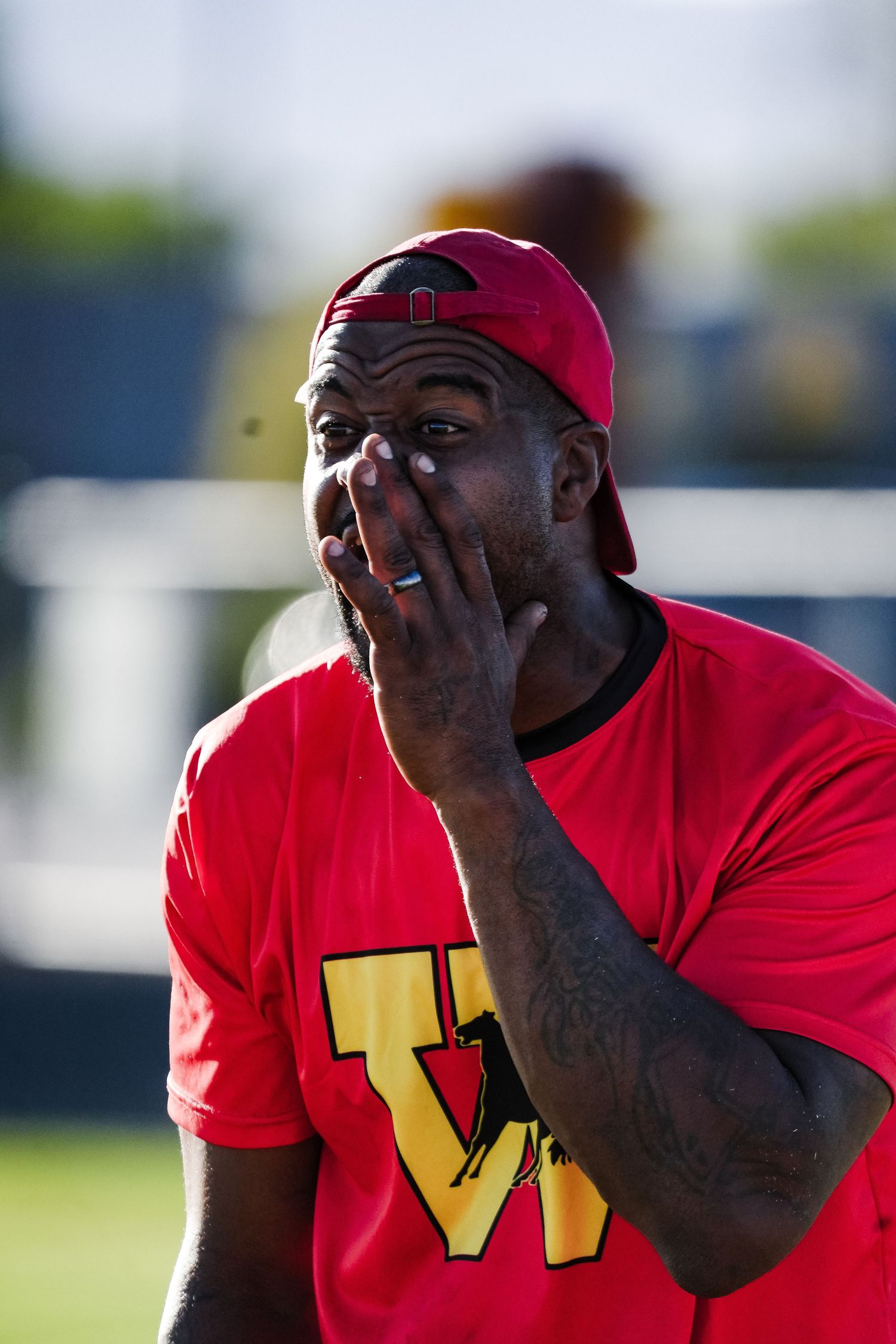 Man in red Washington shirt and cap covers mouth with hand outdoors.