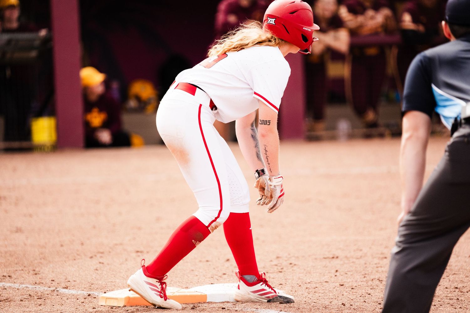 Female softball player in red uniform leading off base during college softball game.