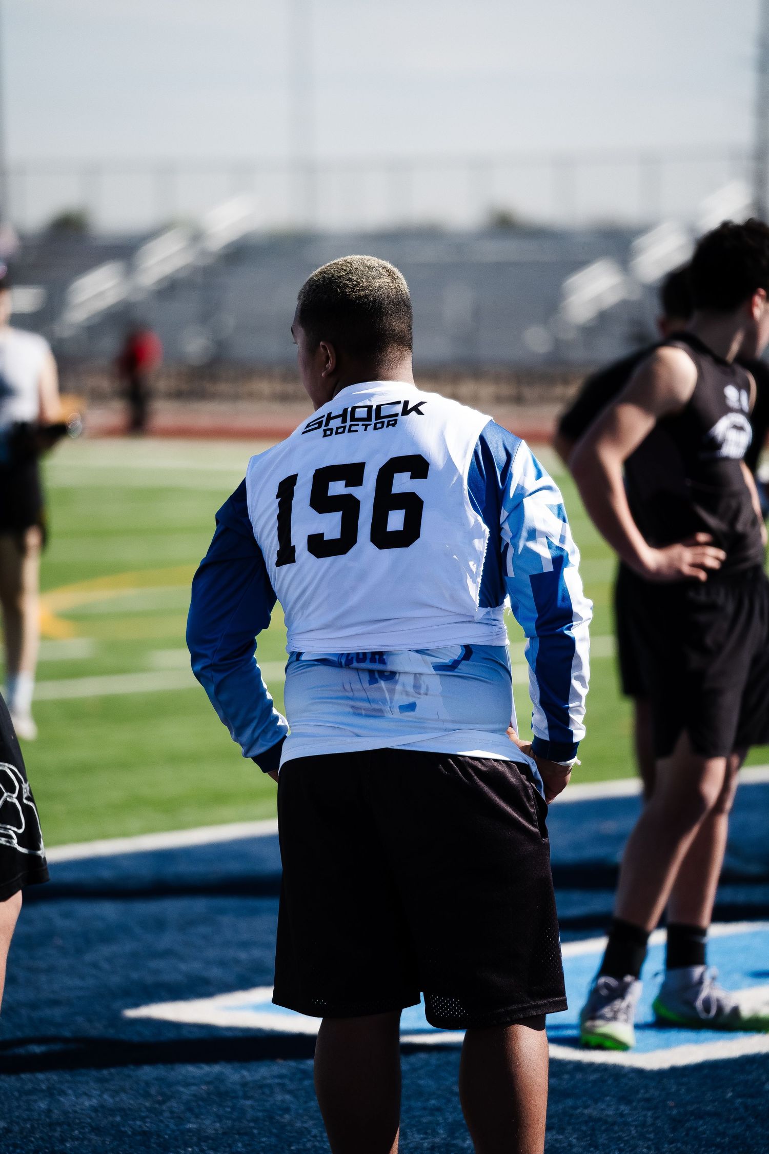 Football player #156 in Shock Boston jersey stands on field during outdoor sports combine event.