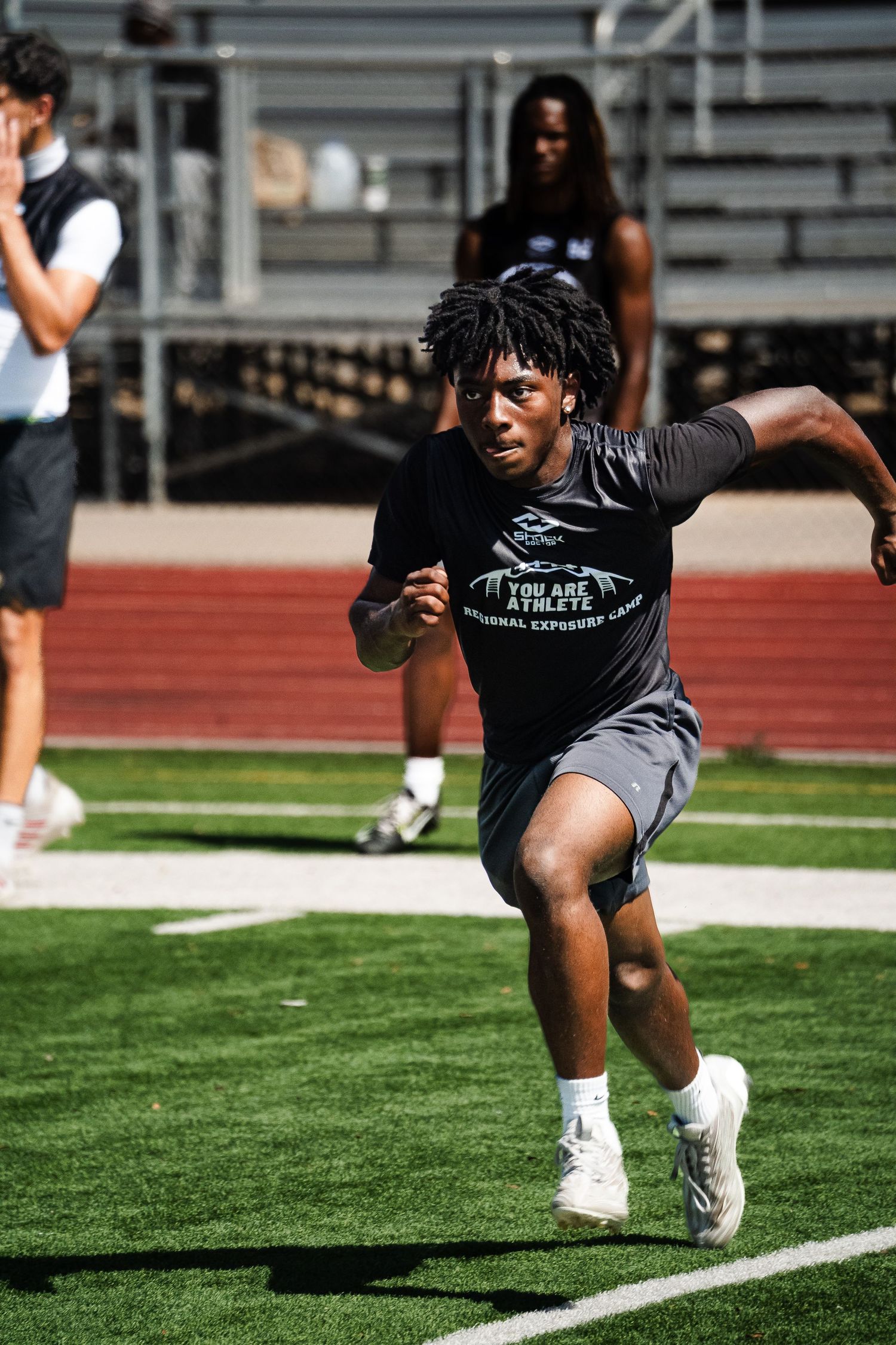 Young athlete in You Are Athlete shirt sprints during a football training camp drill on a turf field.